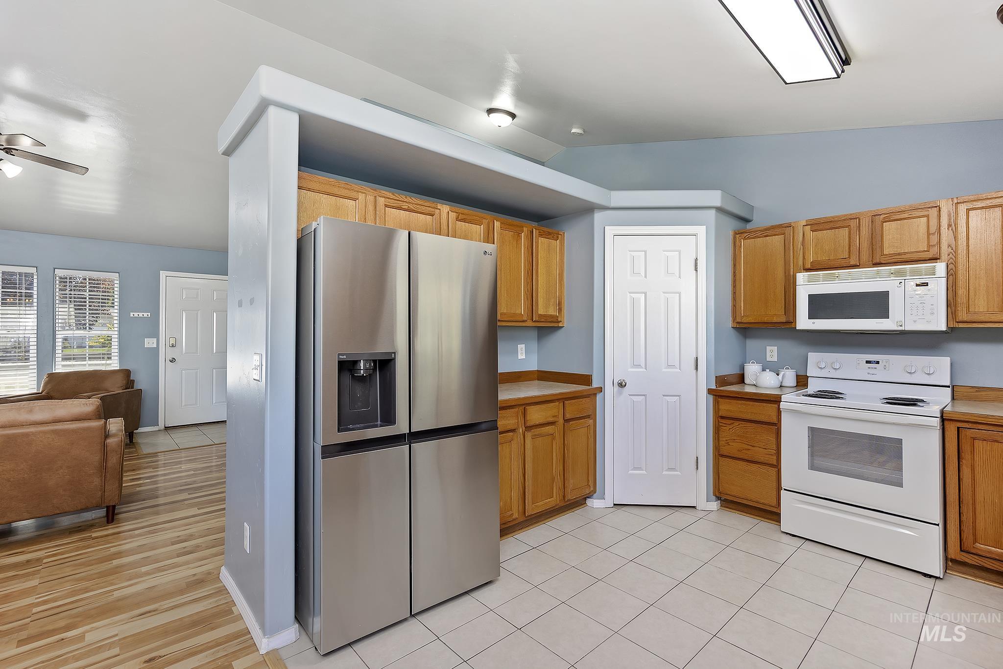 Kitchen with white appliances, light countertops, light tile patterned flooring, brown cabinetry, and ceiling fan