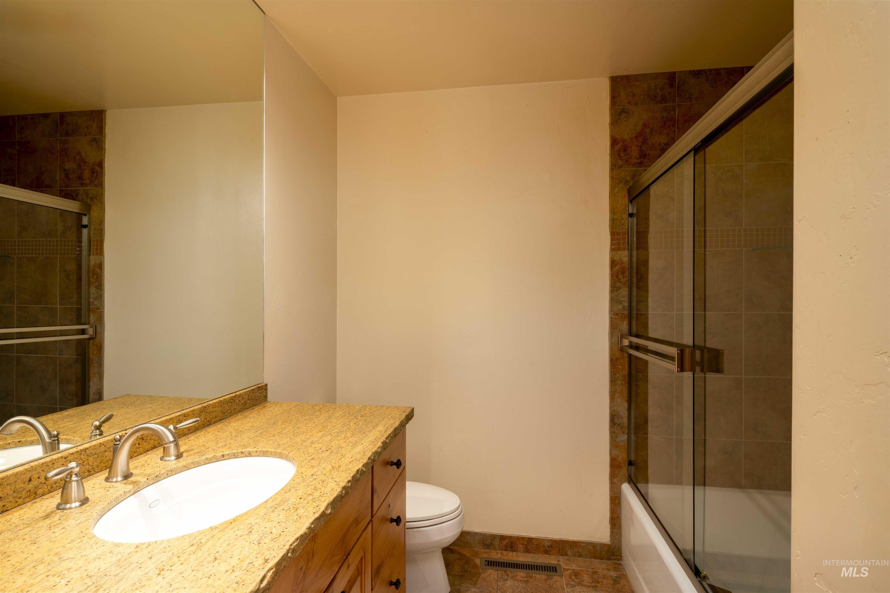 Bathroom featuring vanity, shower / bath combination with glass door, and stone tile flooring