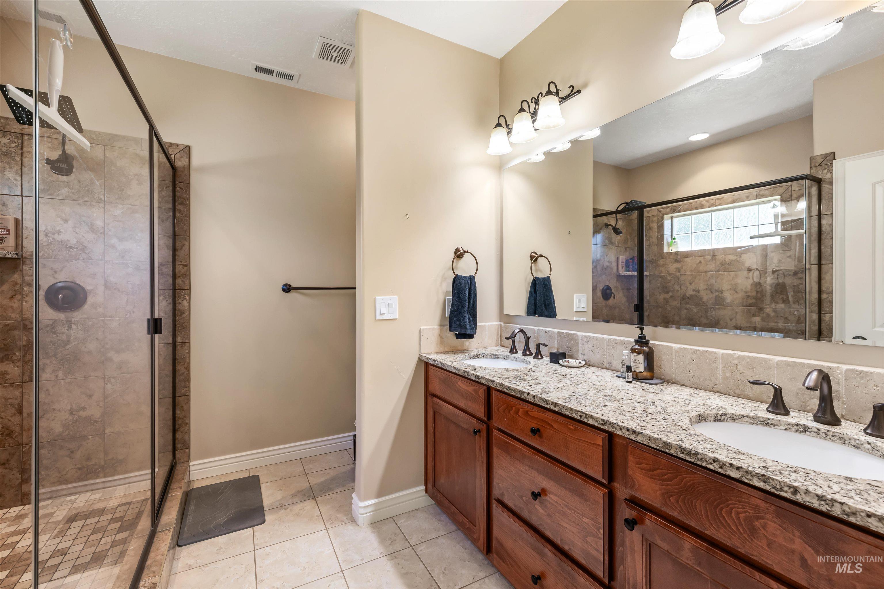 Bathroom featuring a shower stall, light tile patterned floors, and double vanity