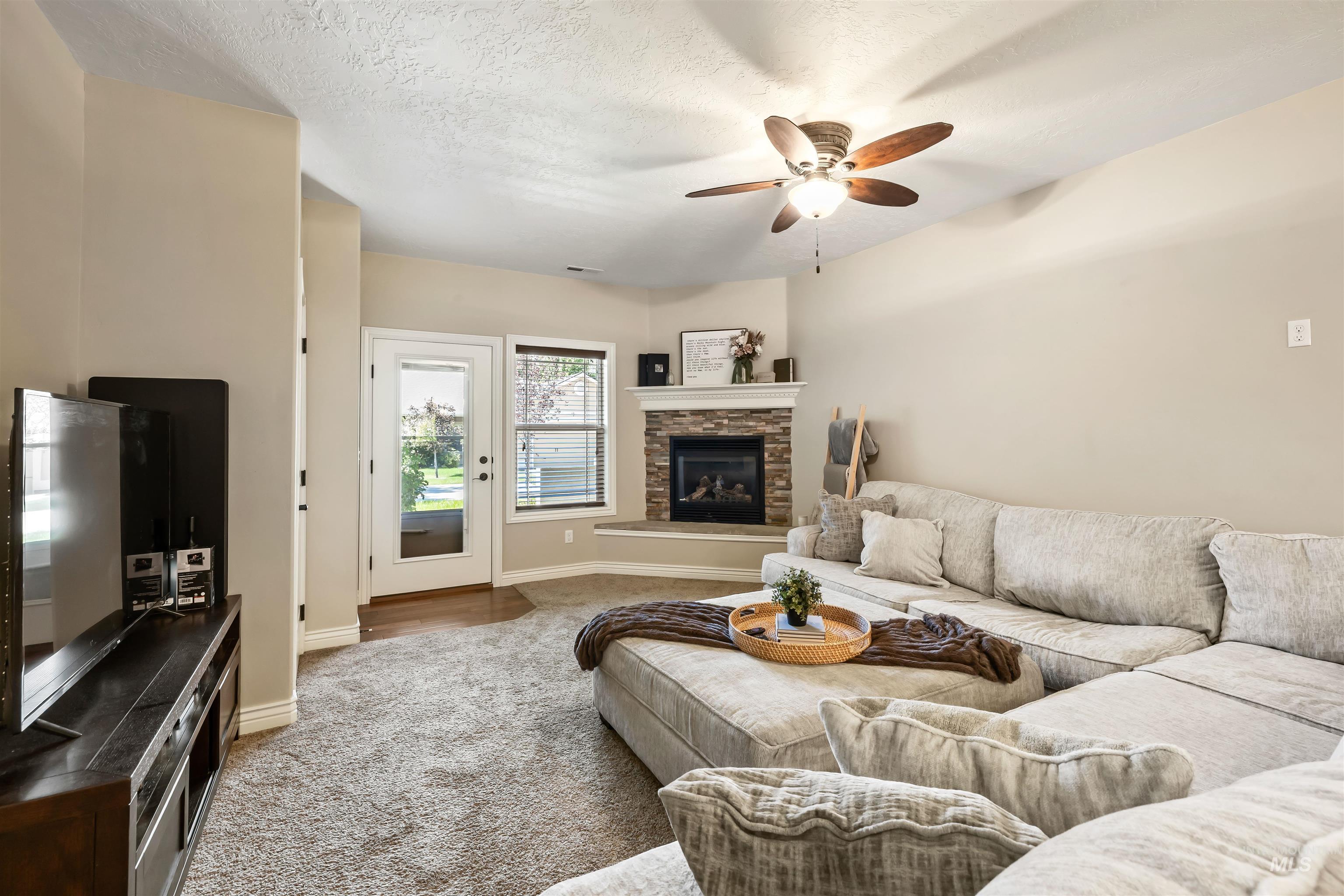 Carpeted living room with ceiling fan, a stone fireplace, and a textured ceiling