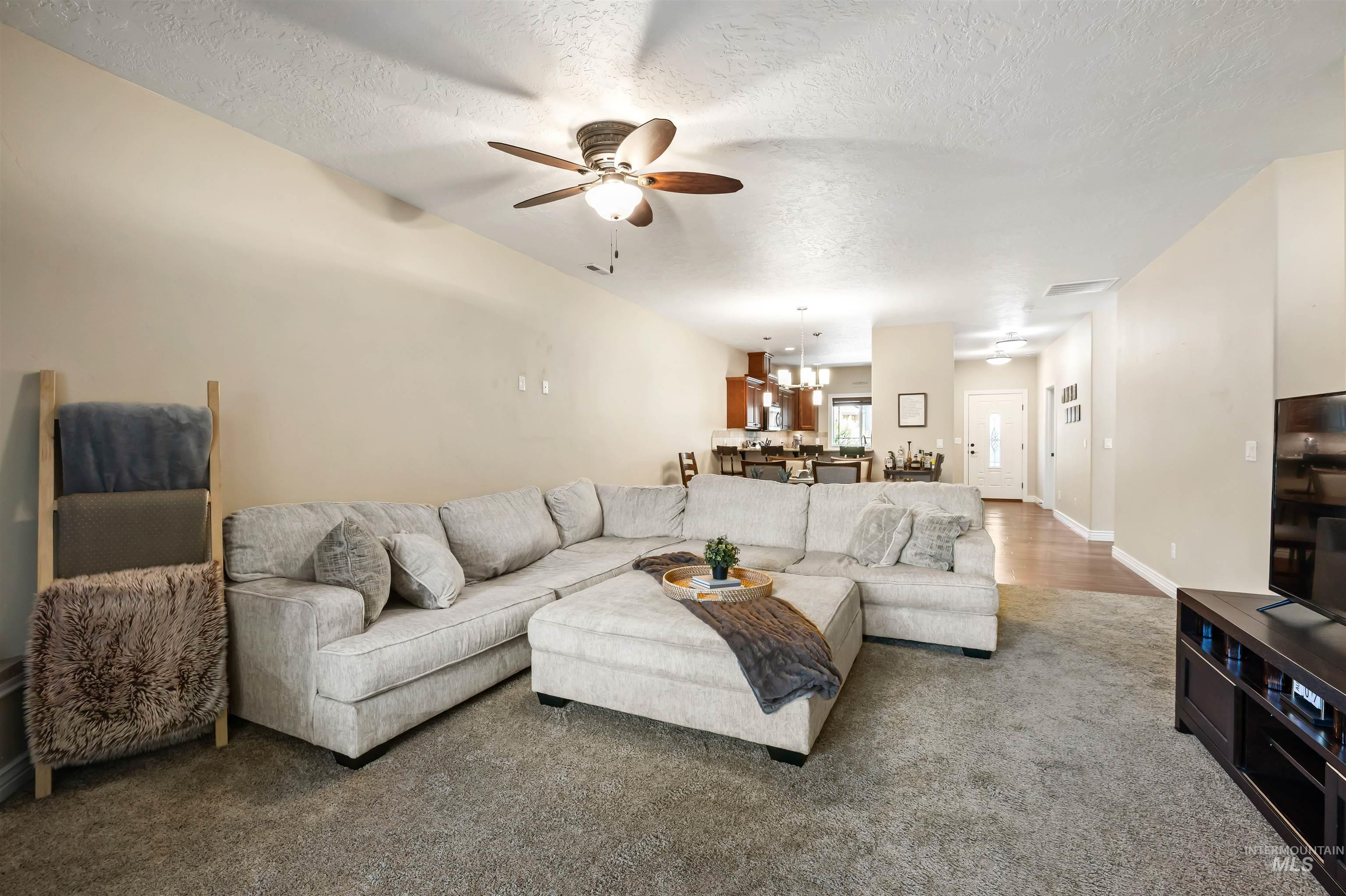 Carpeted living area with ceiling fan, a textured ceiling, and a chandelier