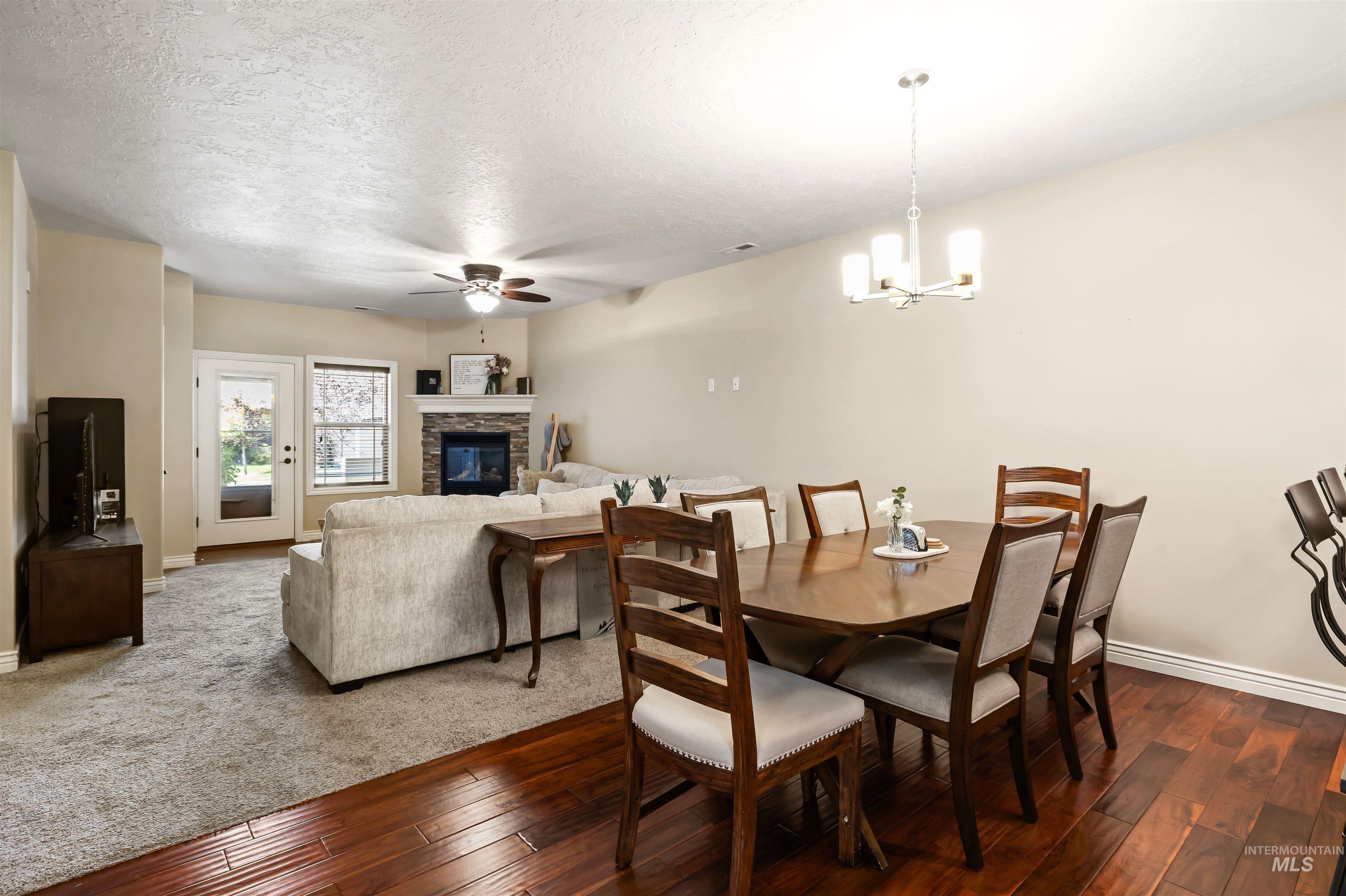 Dining room featuring hardwood / wood-style flooring, ceiling fan, a fireplace, a textured ceiling, and a chandelier