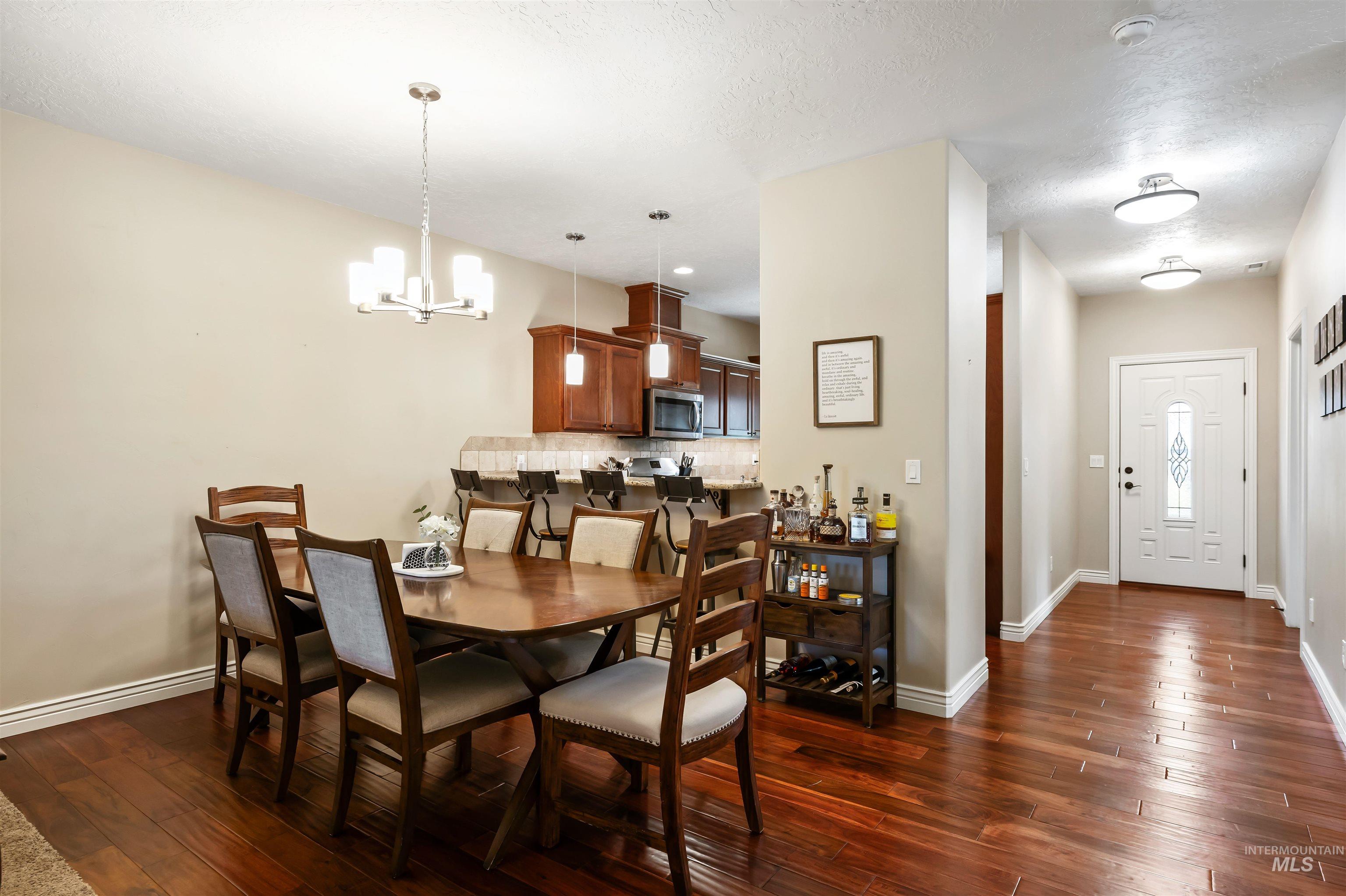 Dining area with dark wood-style flooring, a chandelier, and a textured ceiling