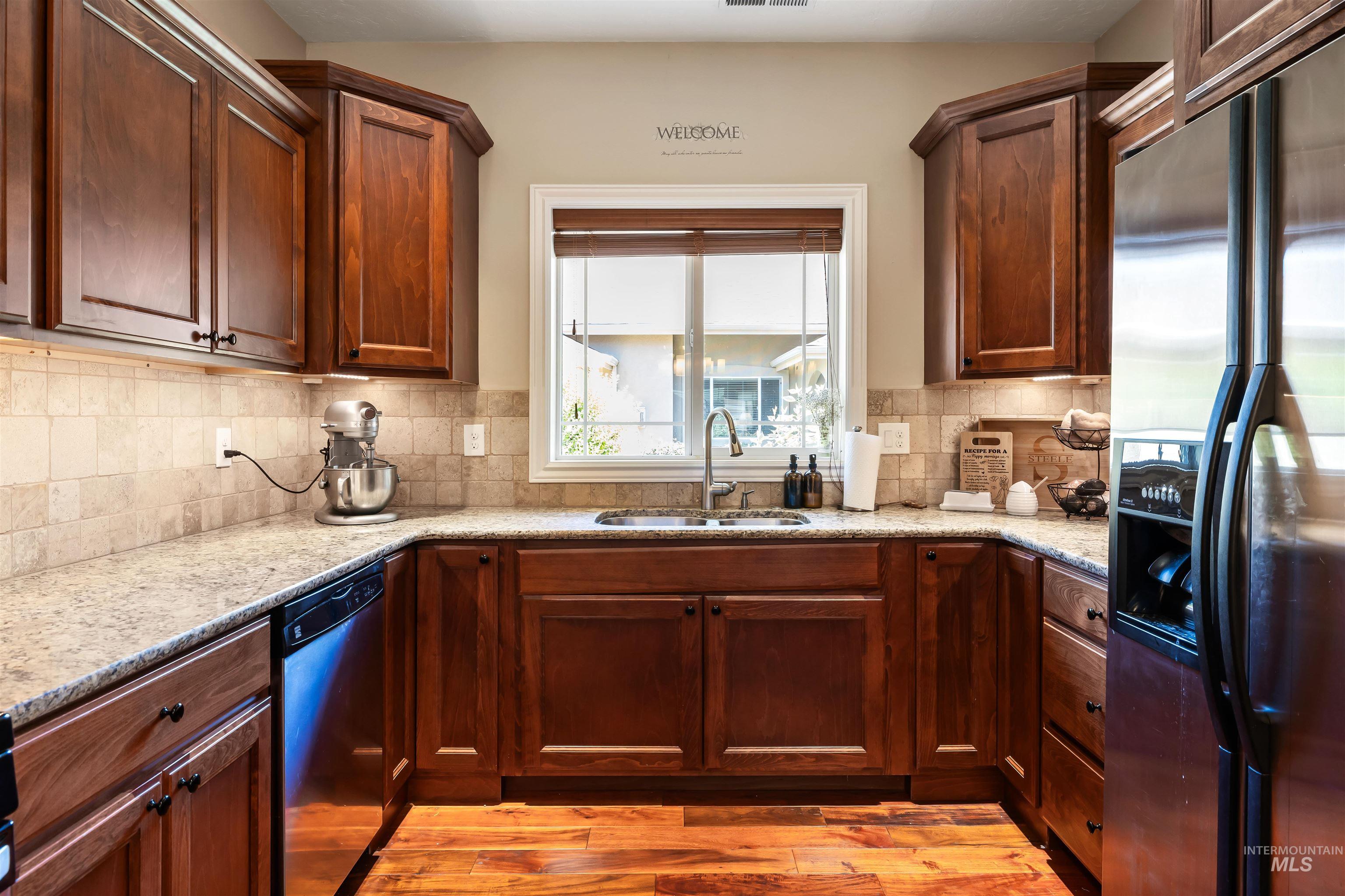 Kitchen with stainless steel refrigerator with ice dispenser, light wood-type flooring, light stone countertops, dishwasher, and tasteful backsplash