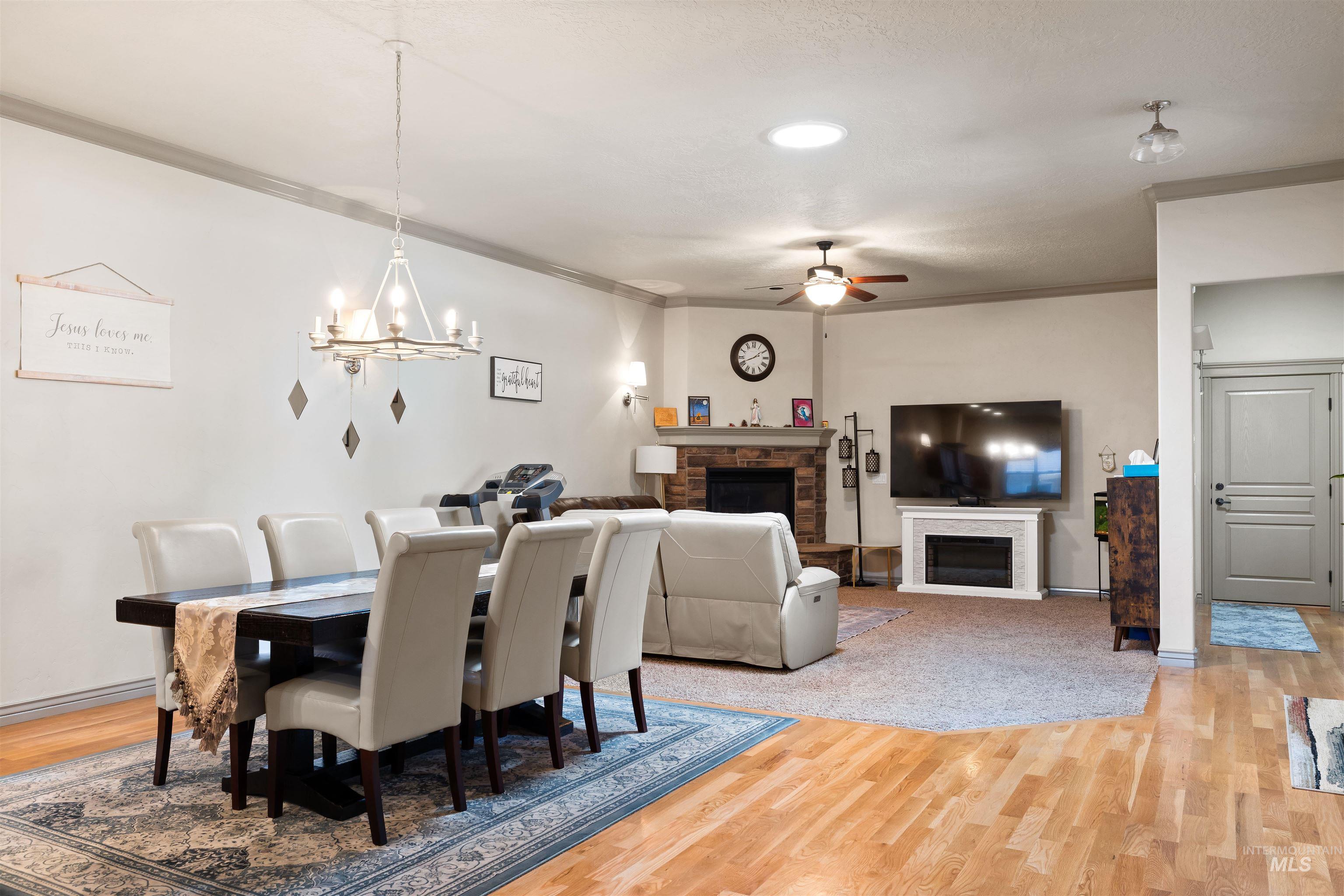 Dining space with a fireplace, light wood-style floors, ornamental molding, ceiling fan, and a chandelier