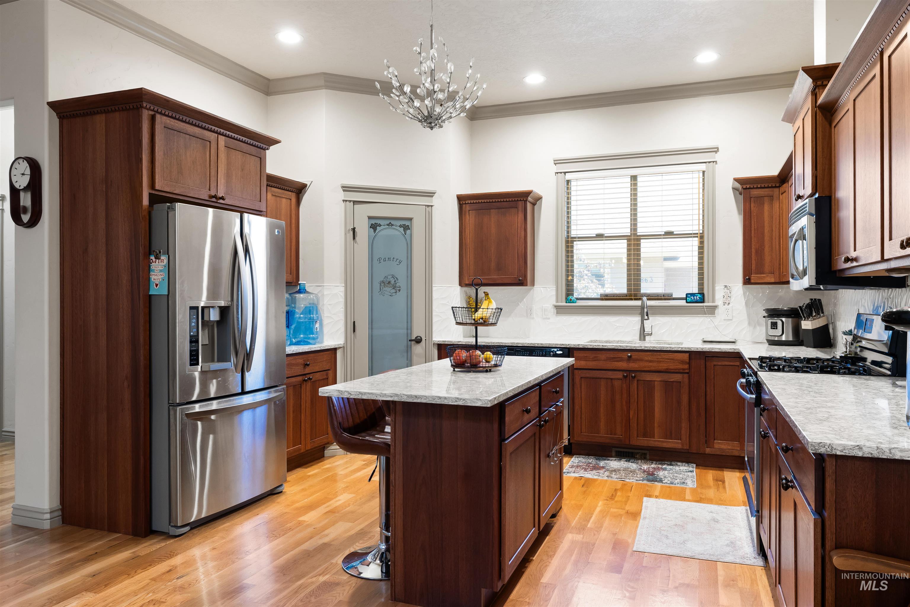 Kitchen with stainless steel appliances, tasteful backsplash, ornamental molding, light wood-type flooring, and a center island