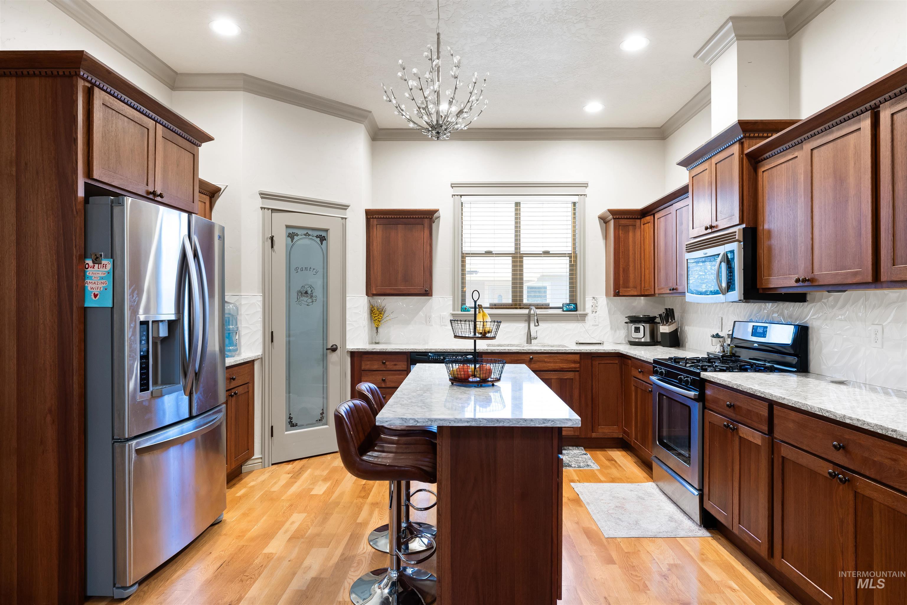 Kitchen featuring appliances with stainless steel finishes, backsplash, light wood finished floors, light stone countertops, and pendant lighting