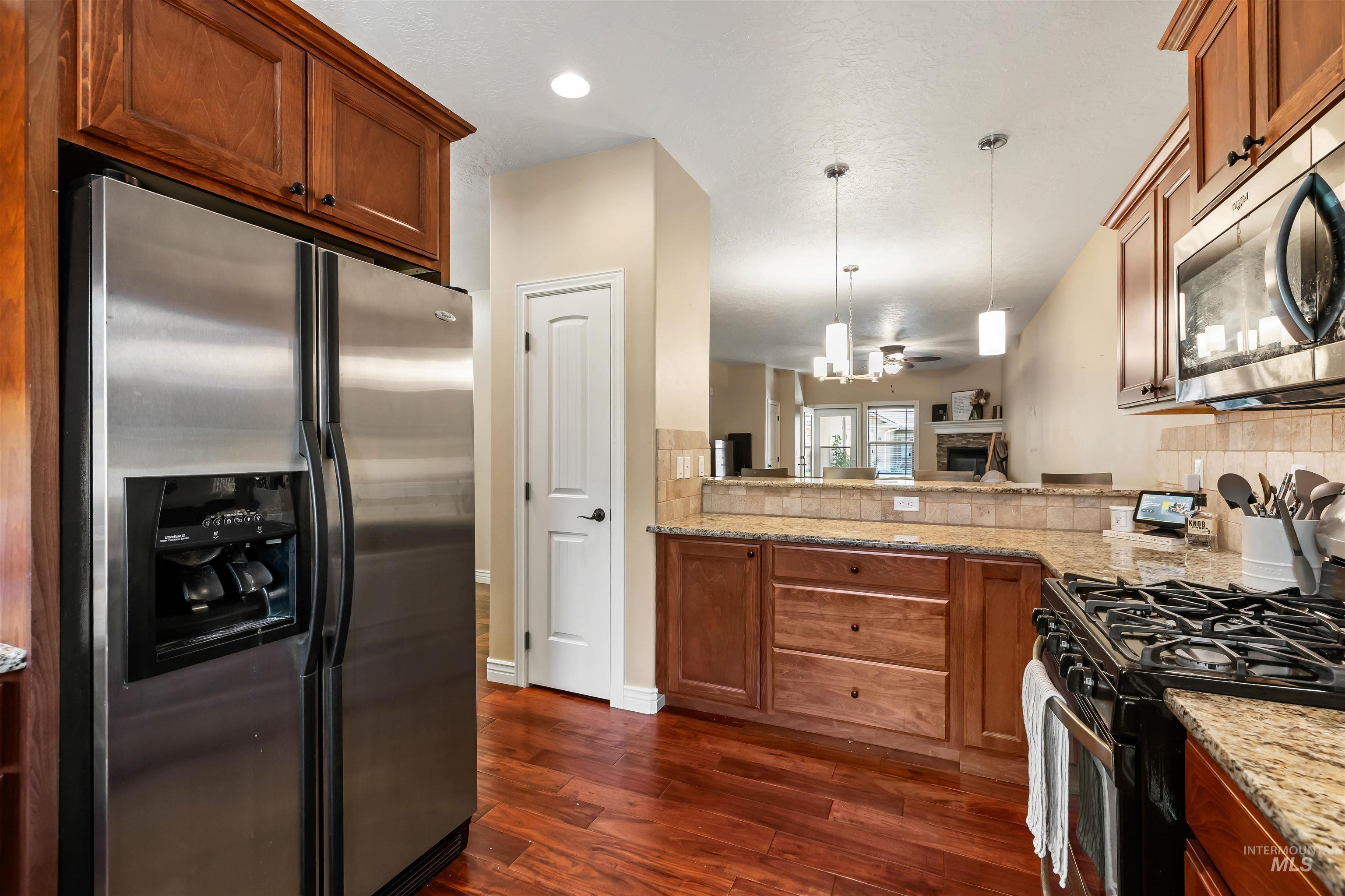 Kitchen featuring stainless steel appliances, decorative light fixtures, a fireplace, light stone countertops, and backsplash