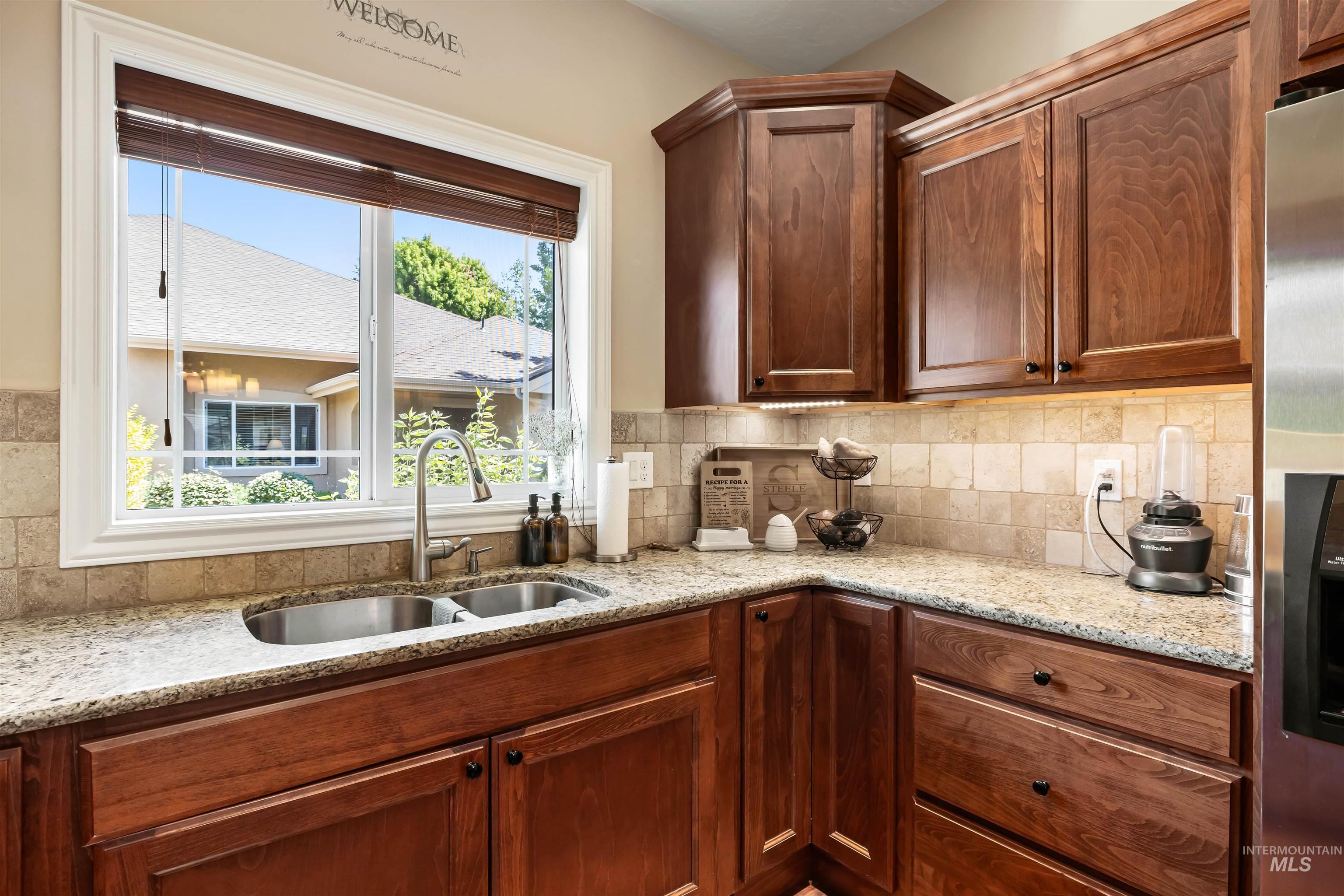Kitchen featuring light stone countertops, stainless steel refrigerator with ice dispenser, and tasteful backsplash
