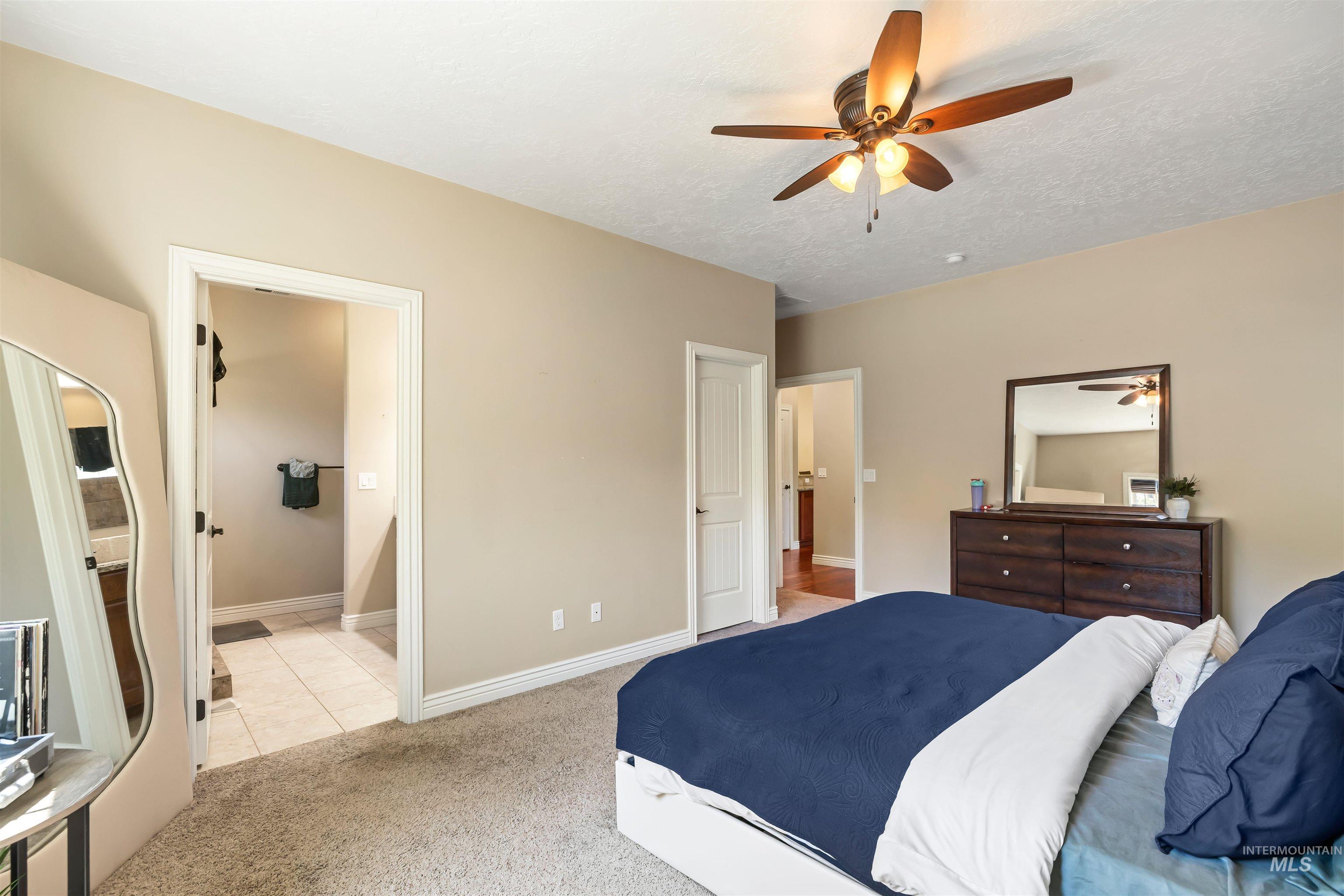 Bedroom with light carpet, ensuite bathroom, a ceiling fan, and light tile patterned floors