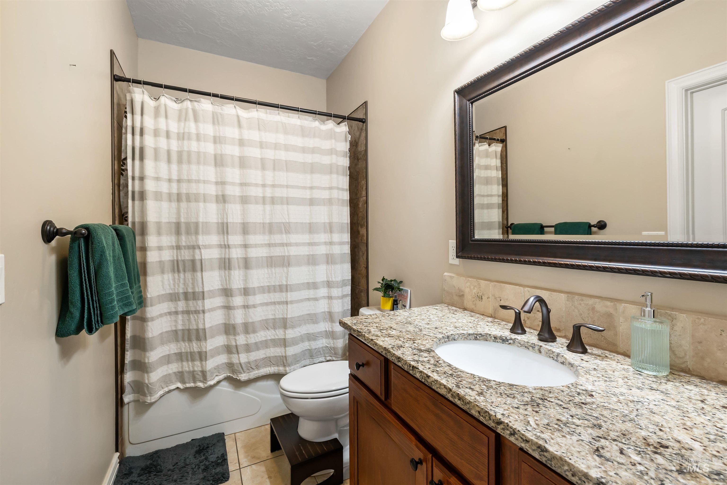 Bathroom featuring shower / bathtub combination with curtain, vanity, light tile patterned flooring, and a textured ceiling