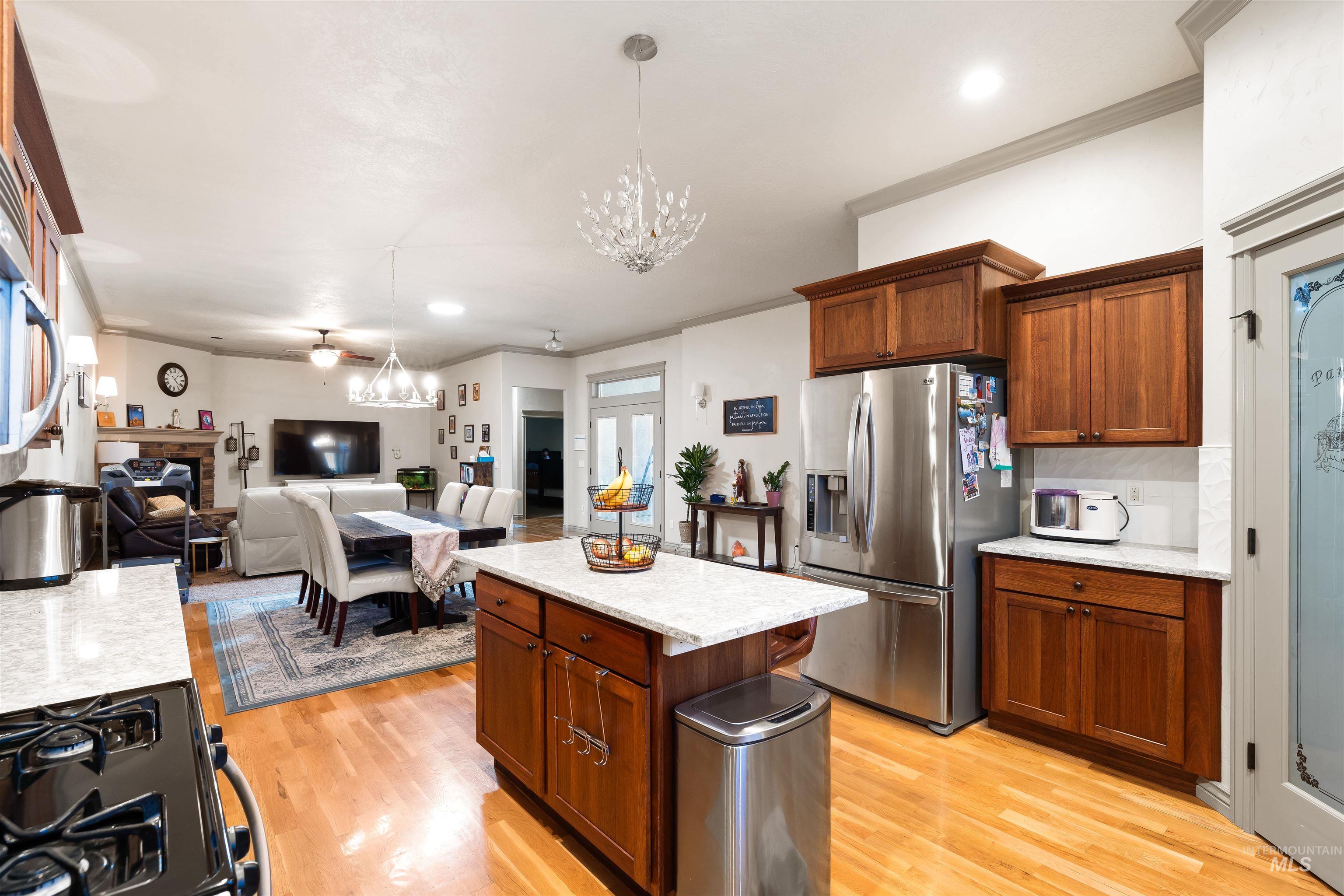 Kitchen featuring brown cabinetry, ornamental molding, stainless steel fridge, black range with gas stovetop, and light wood-style floors