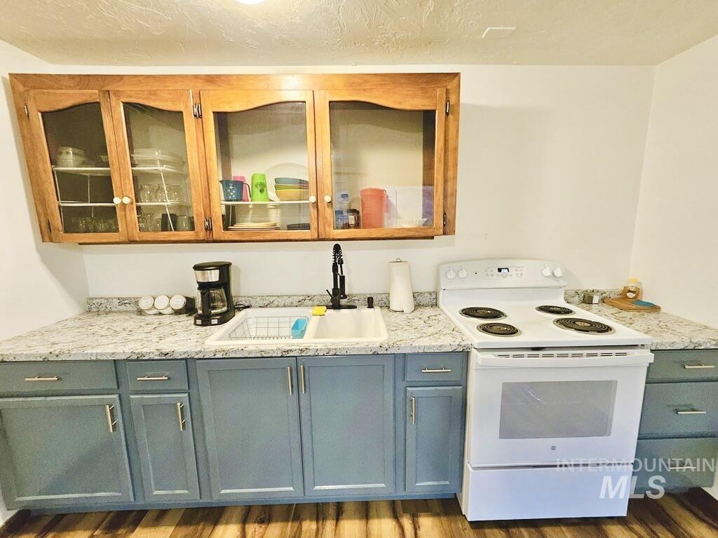 Kitchen featuring white range with electric cooktop, wood finished floors, light stone countertops, glass insert cabinets, and a textured ceiling