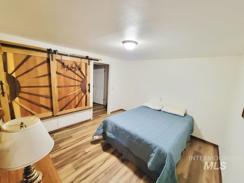 Bedroom featuring light wood-type flooring, a barn door, and a textured ceiling