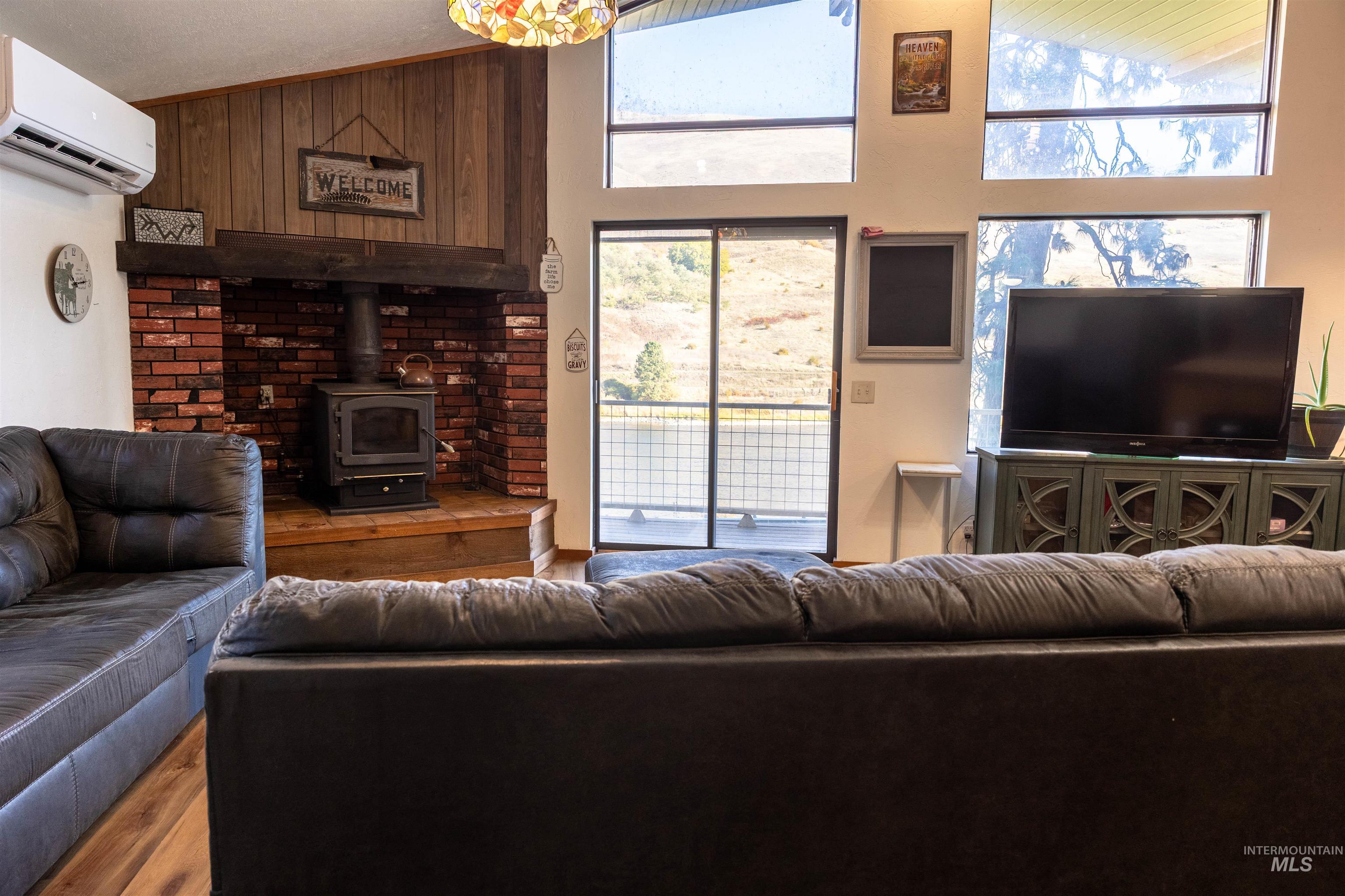 Living area featuring a wood stove, wood finished floors, a wall mounted air conditioner, wooden walls, and high vaulted ceiling