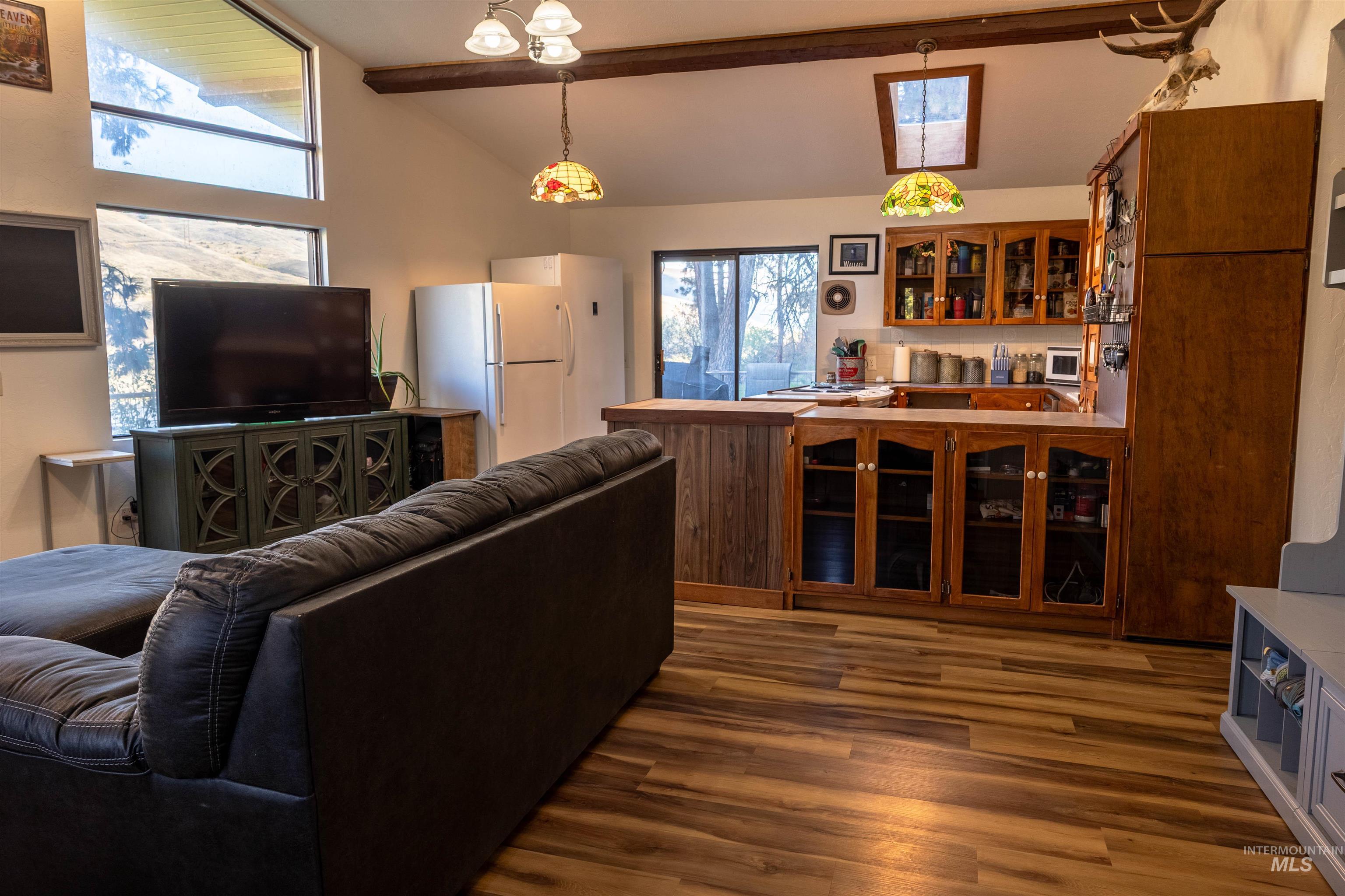 Living room featuring beamed ceiling, dark wood-type flooring, a skylight, and high vaulted ceiling