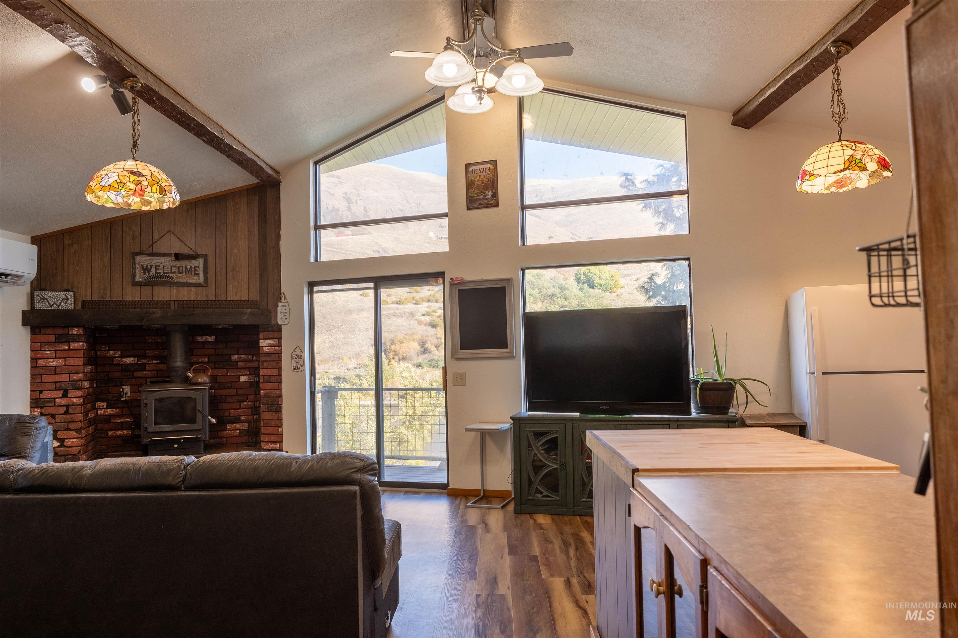 Living area featuring beam ceiling, a wood stove, dark wood-style floors, high vaulted ceiling, and ceiling fan