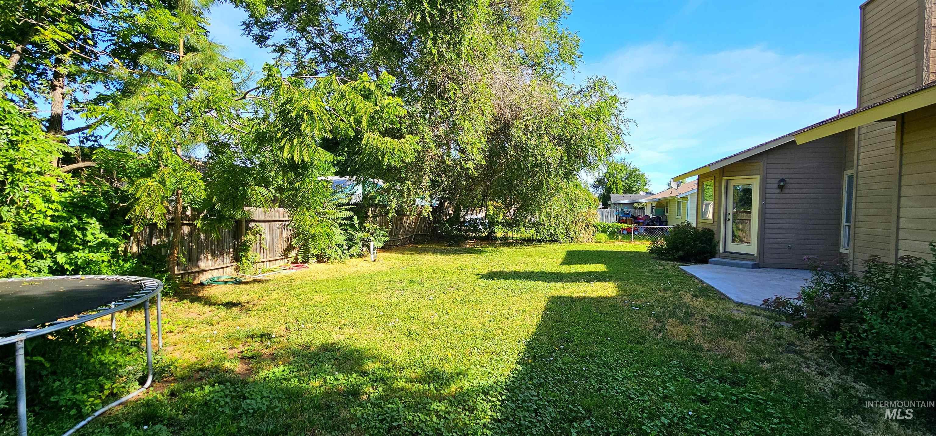 Fenced backyard featuring a trampoline and a patio area