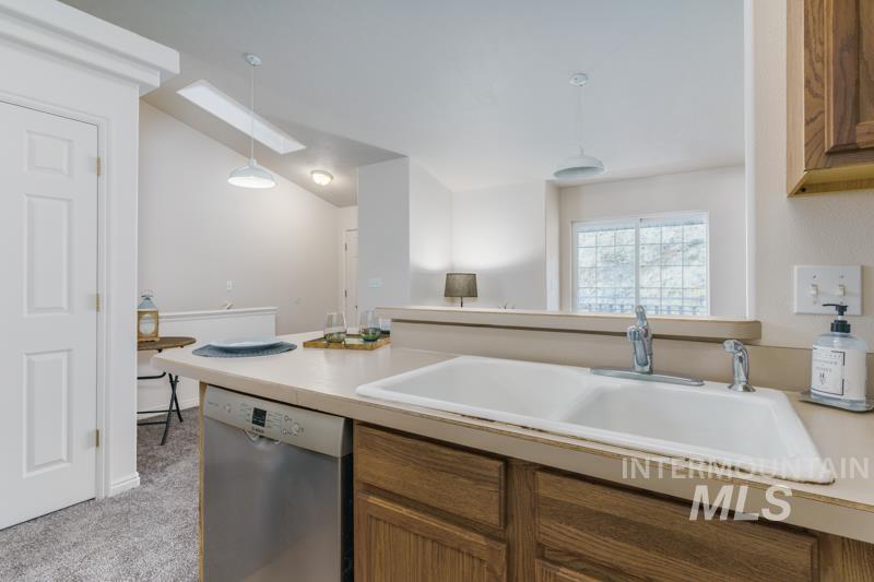Kitchen with brown cabinetry, dishwasher, light countertops, light colored carpet, and hanging light fixtures