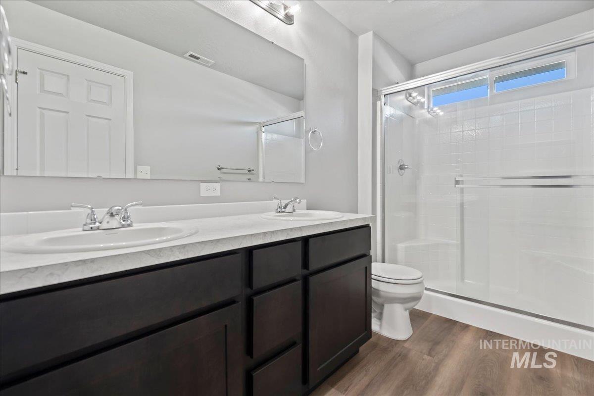 Full bathroom with double vanity, a stall shower, and dark wood finished floors