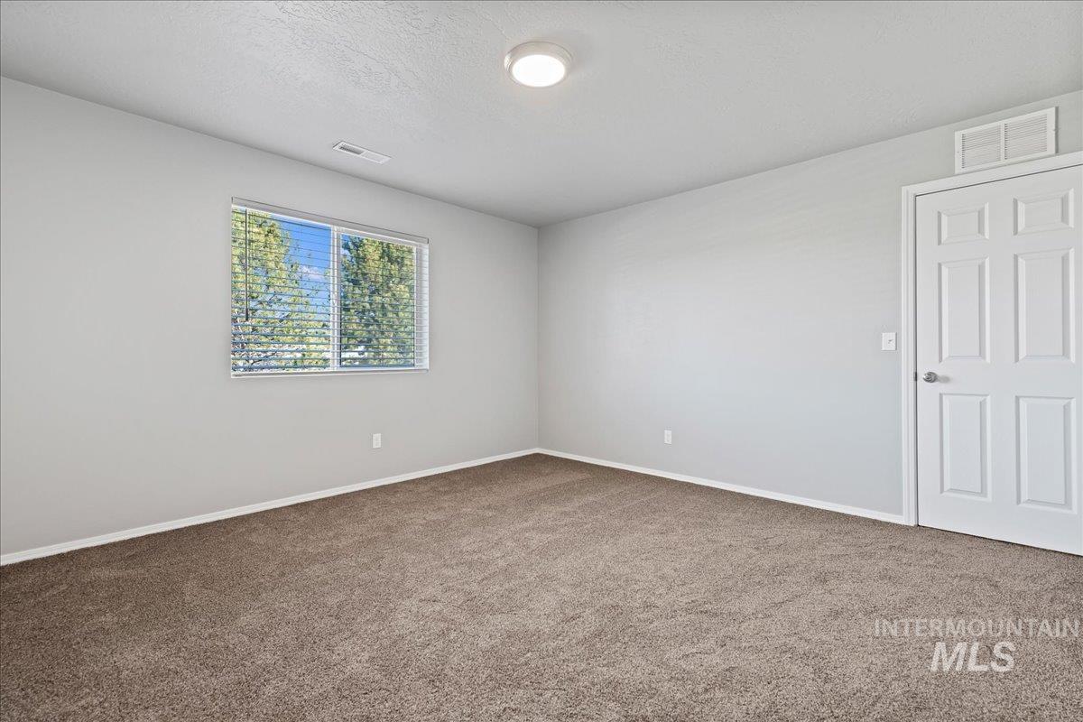 Carpeted spare room featuring a textured ceiling and baseboards