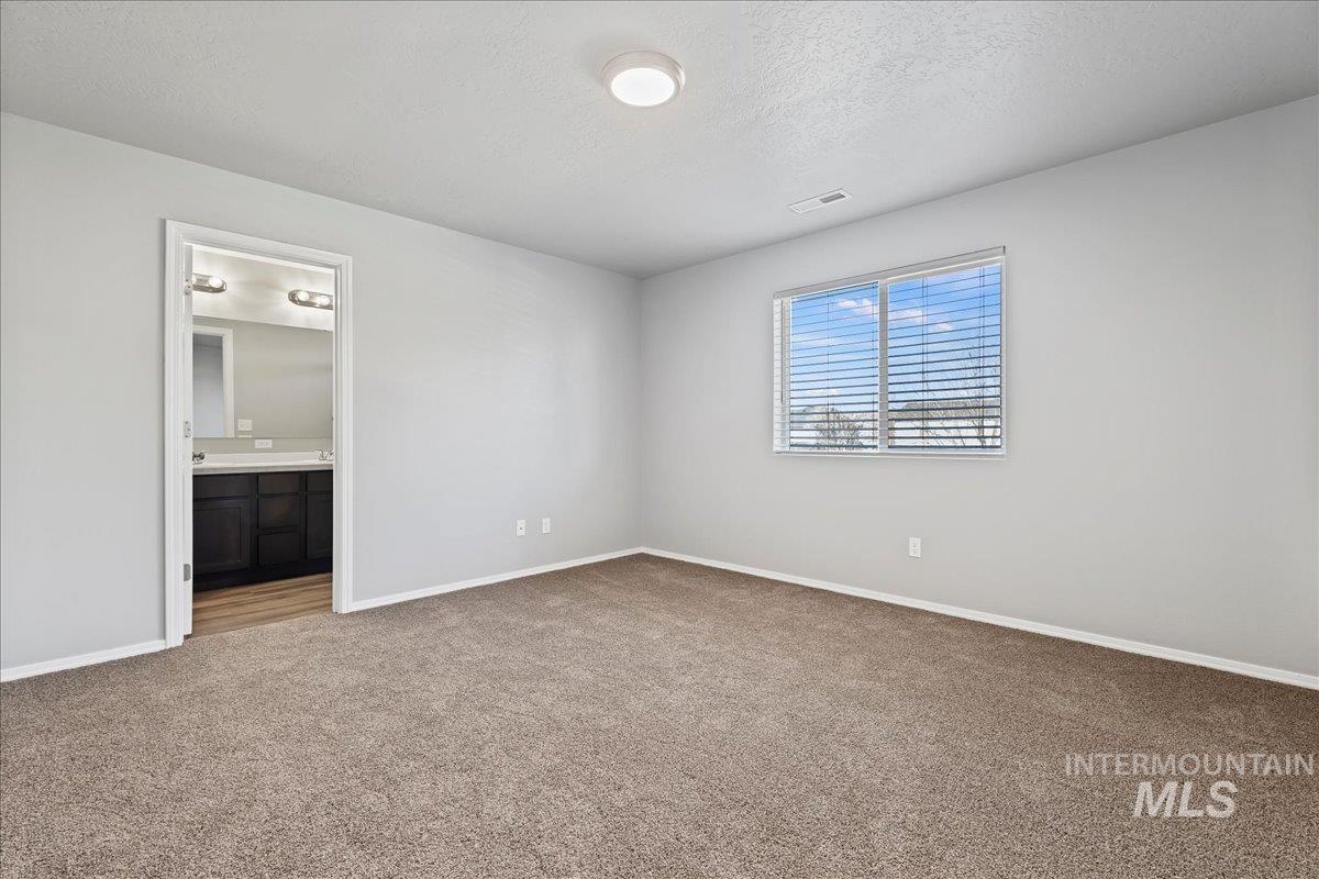 Unfurnished bedroom featuring a textured ceiling, carpet floors, and ensuite bath