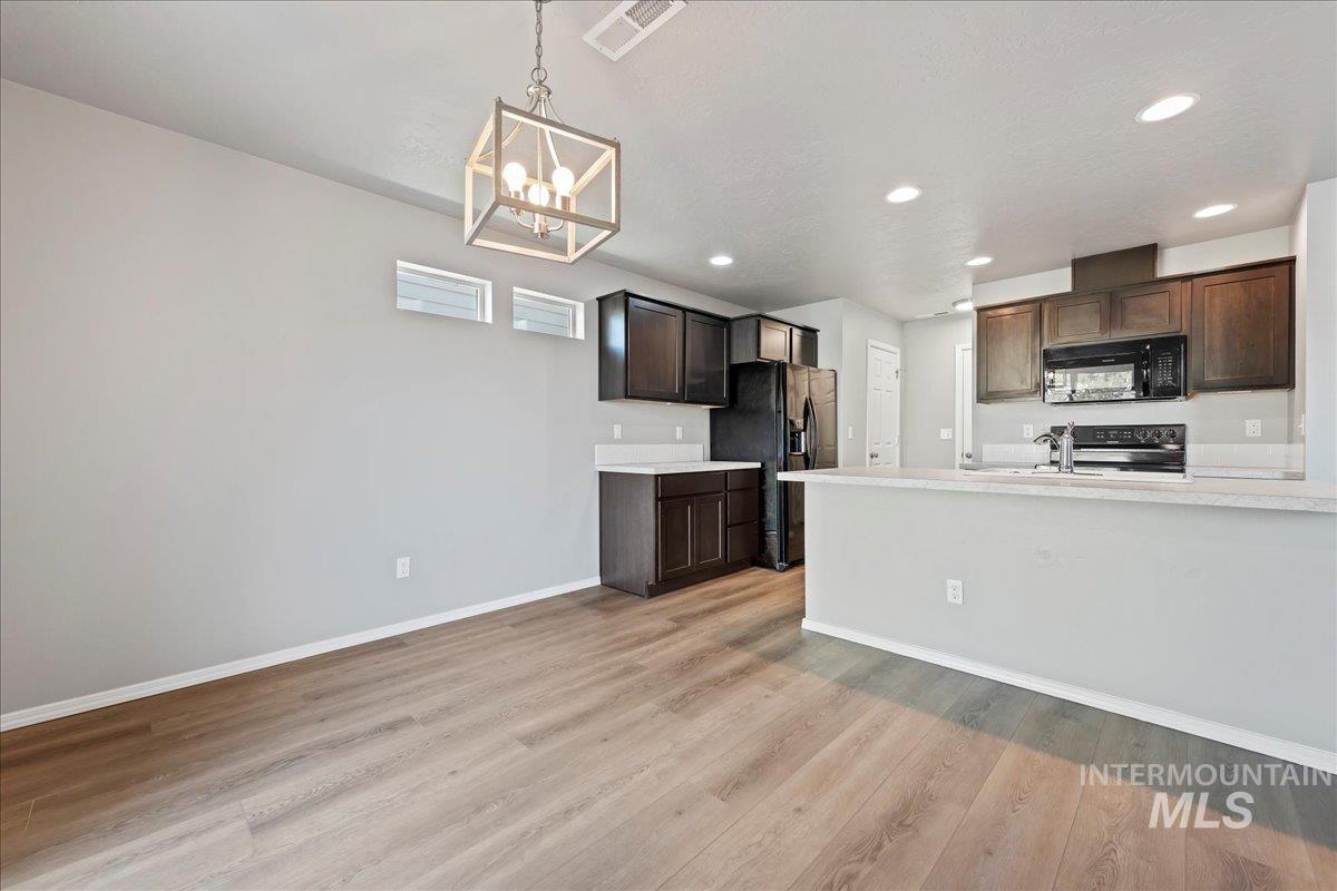 Kitchen featuring light countertops, dark brown cabinetry, black appliances, hanging light fixtures, and recessed lighting