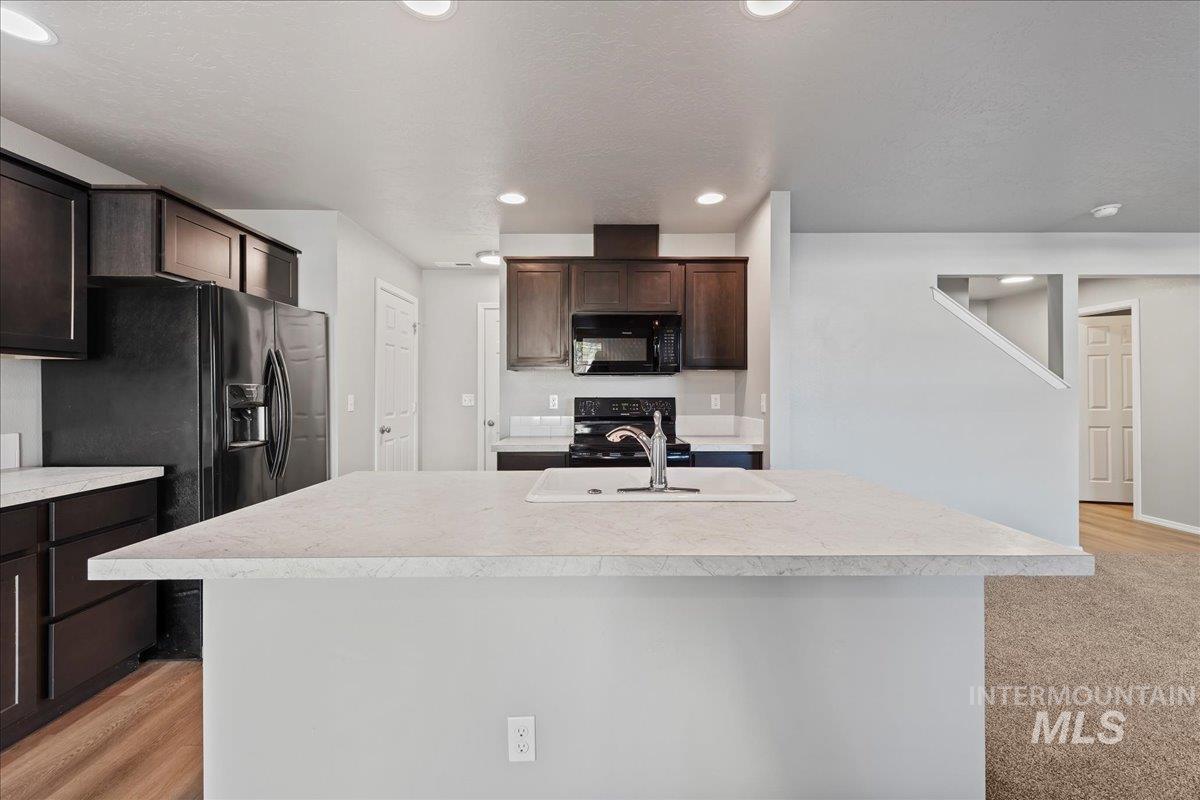 Kitchen featuring dark brown cabinetry, light countertops, a kitchen island with sink, black appliances, and recessed lighting