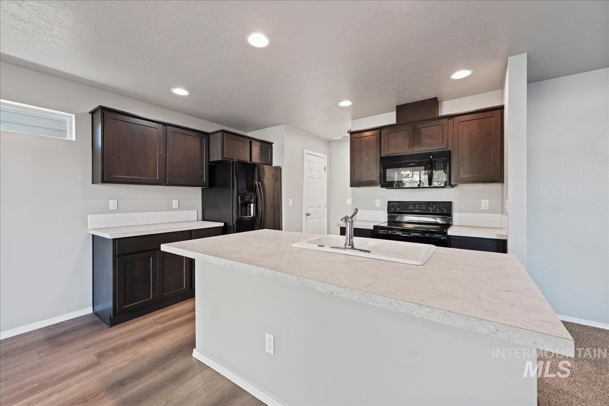Kitchen with light countertops, black appliances, dark brown cabinets, a kitchen island with sink, and recessed lighting