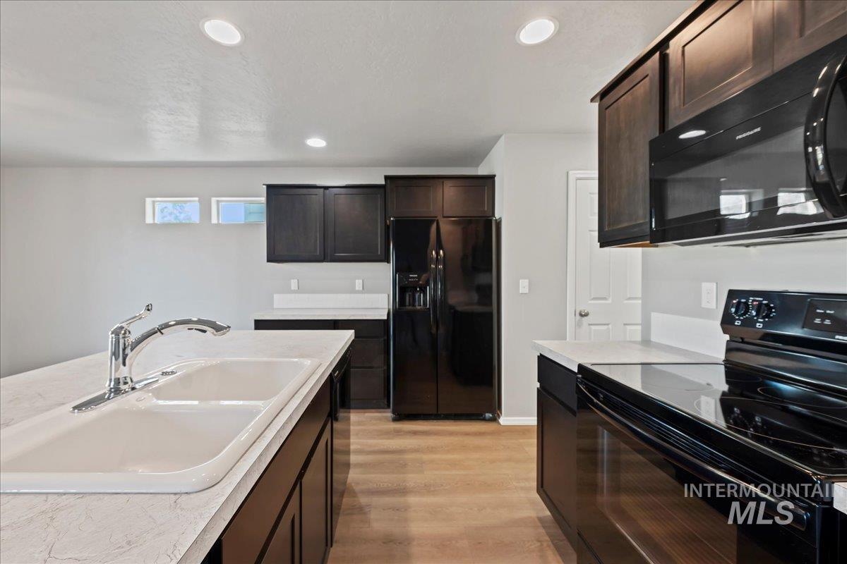Kitchen featuring black appliances, light countertops, recessed lighting, dark brown cabinets, and light wood finished floors