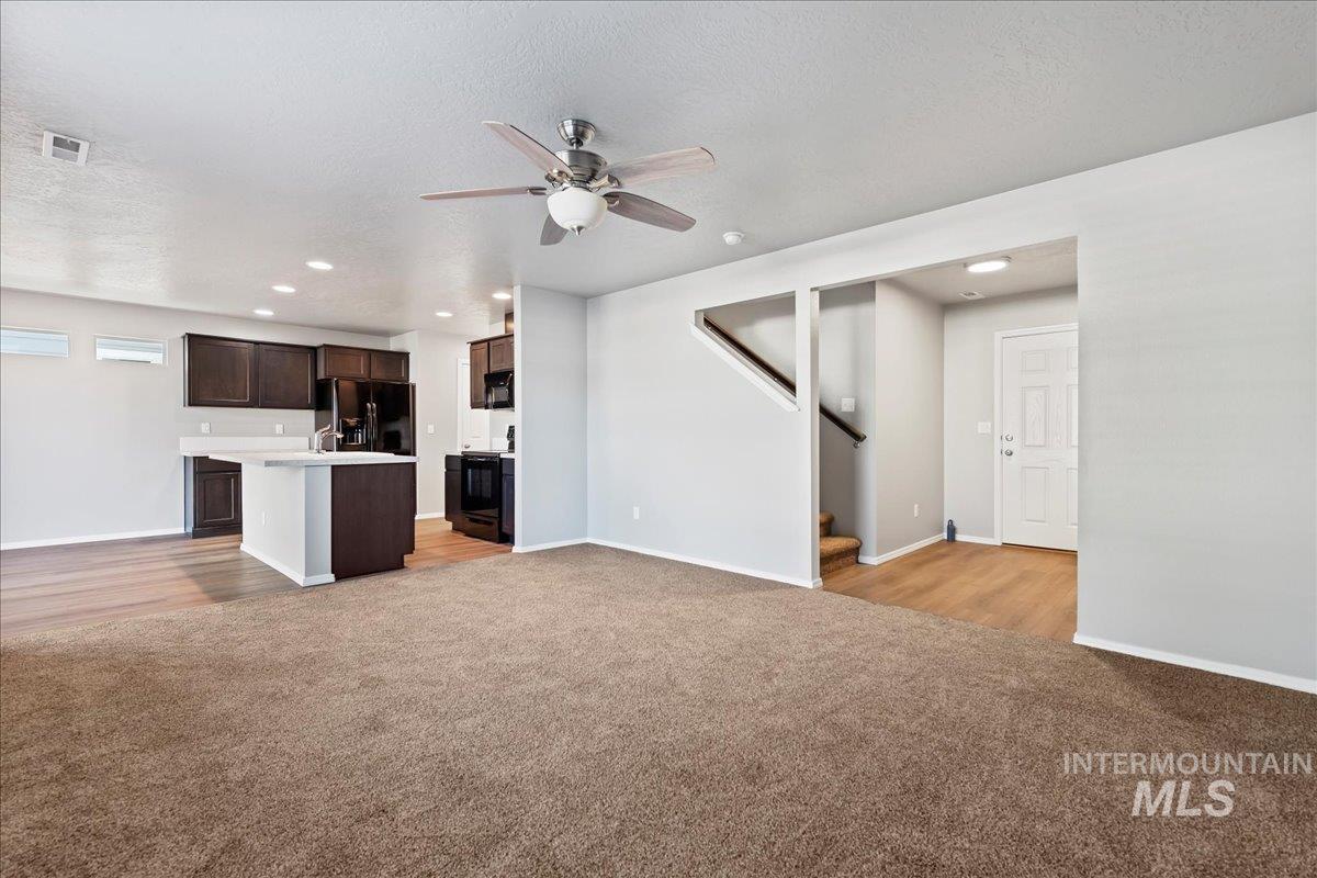 Unfurnished living room with recessed lighting, light carpet, a ceiling fan, stairway, and a textured ceiling