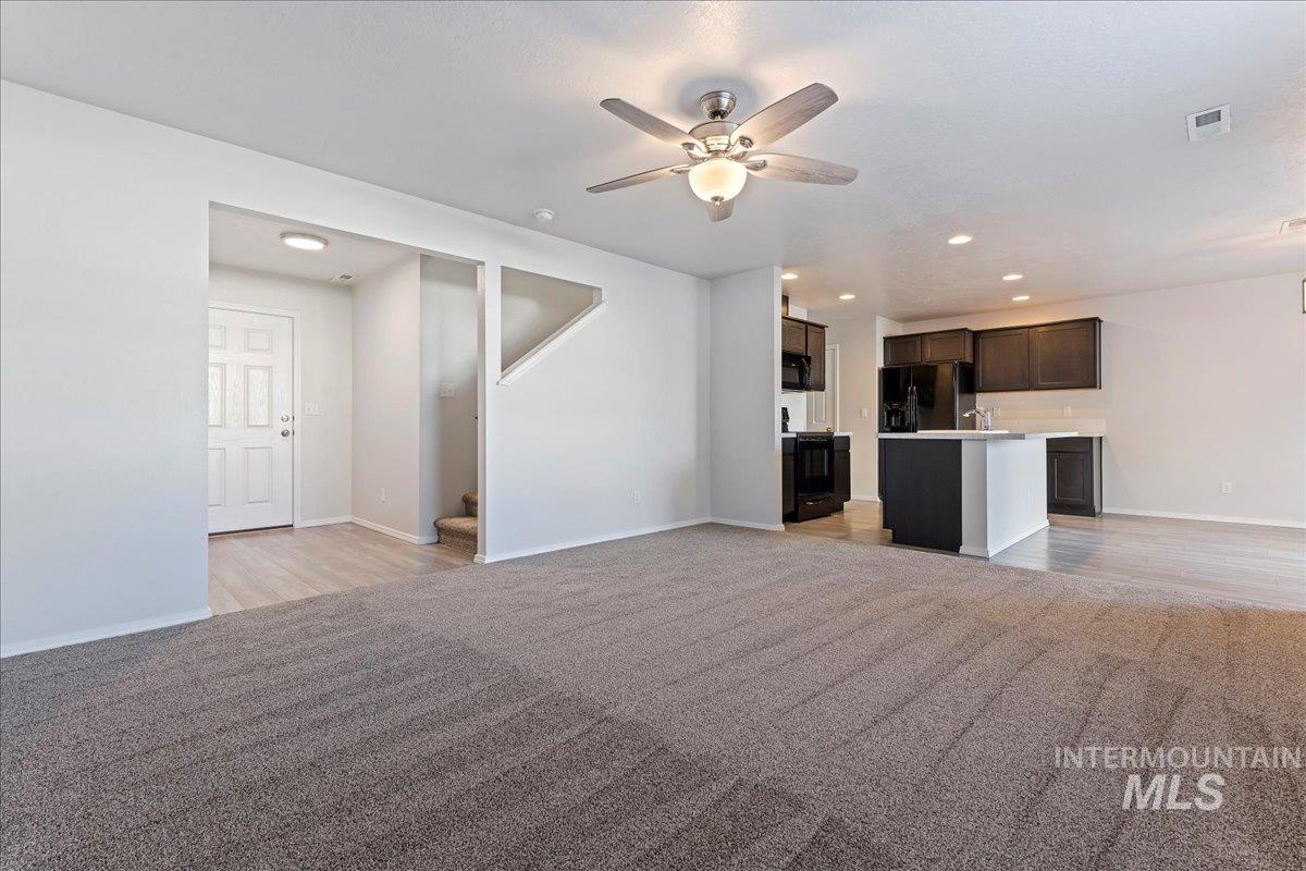 Unfurnished living room featuring light carpet, a ceiling fan, recessed lighting, and stairs