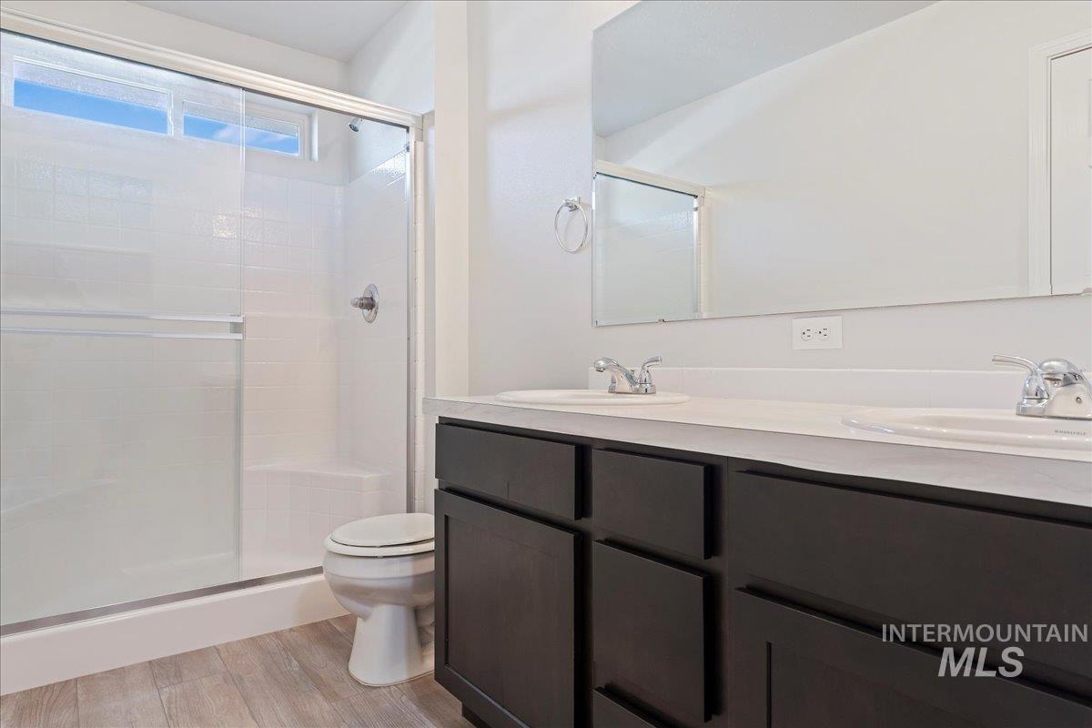 Full bath featuring double vanity, a shower stall, and light wood-style flooring