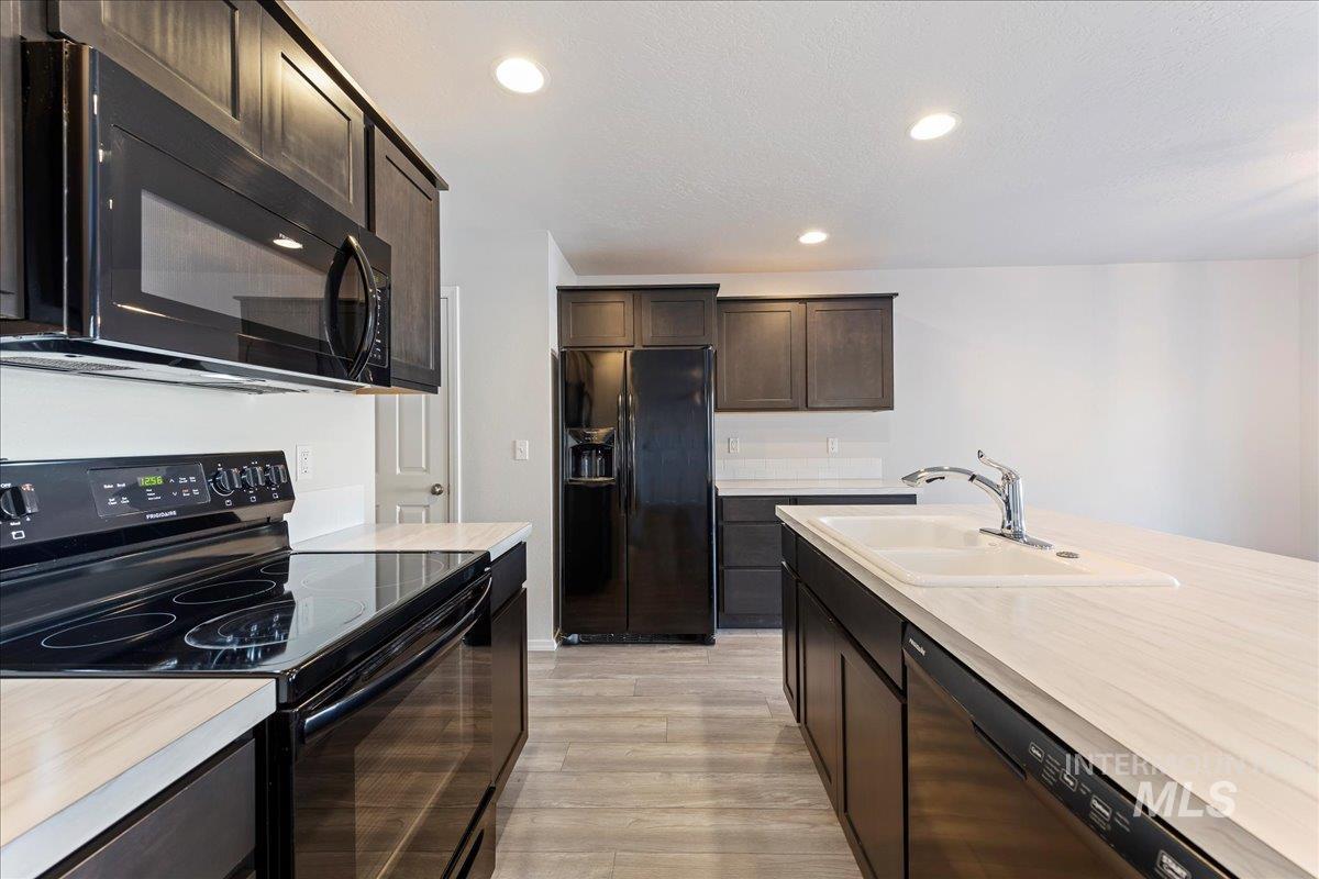 Kitchen with black appliances, recessed lighting, dark brown cabinets, light countertops, and light wood finished floors