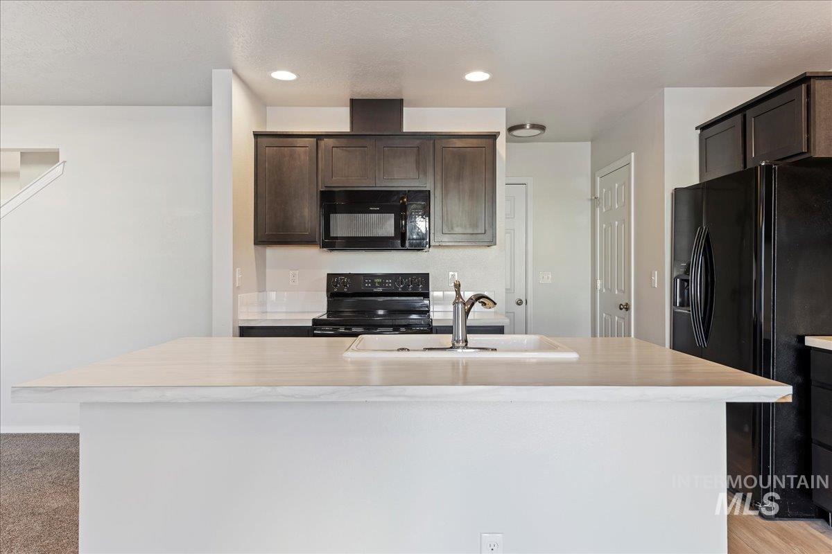 Kitchen with black appliances, light countertops, a center island with sink, dark brown cabinetry, and recessed lighting