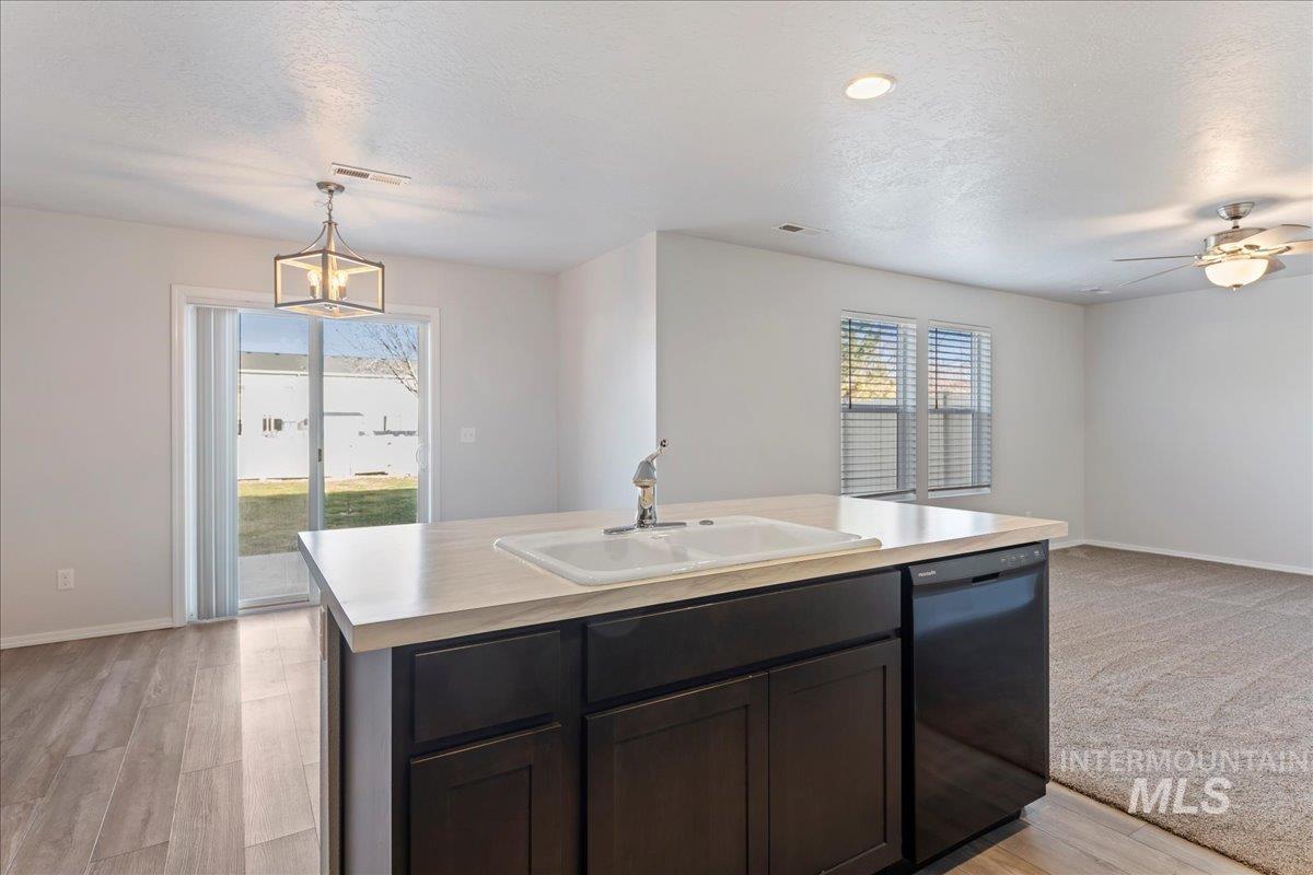 Kitchen featuring open floor plan, light countertops, decorative light fixtures, an island with sink, and a textured ceiling