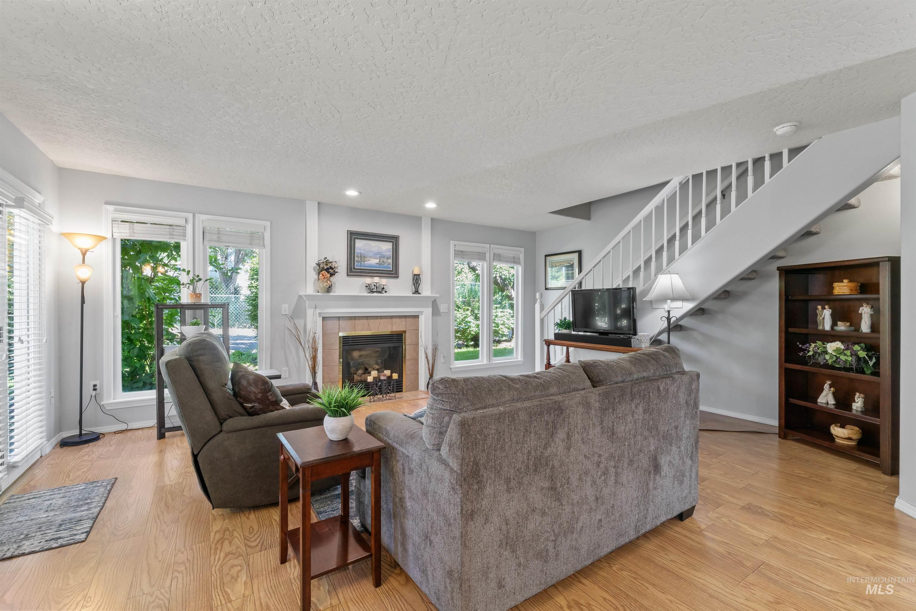 Living room with a textured ceiling, stairs, light wood-style floors, a tile fireplace, and recessed lighting