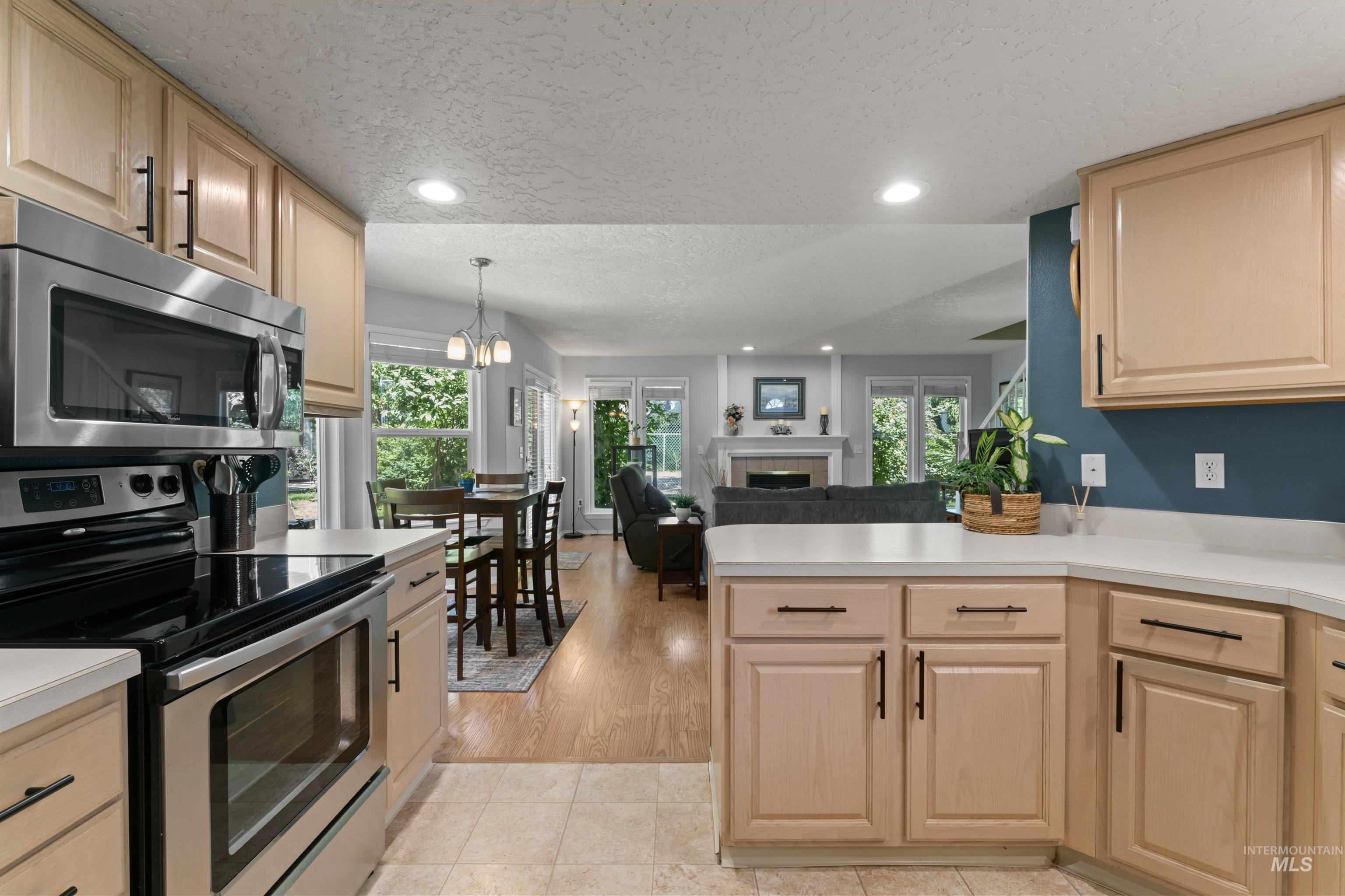 Kitchen with appliances with stainless steel finishes, light brown cabinets, a textured ceiling, a fireplace, and plenty of natural light