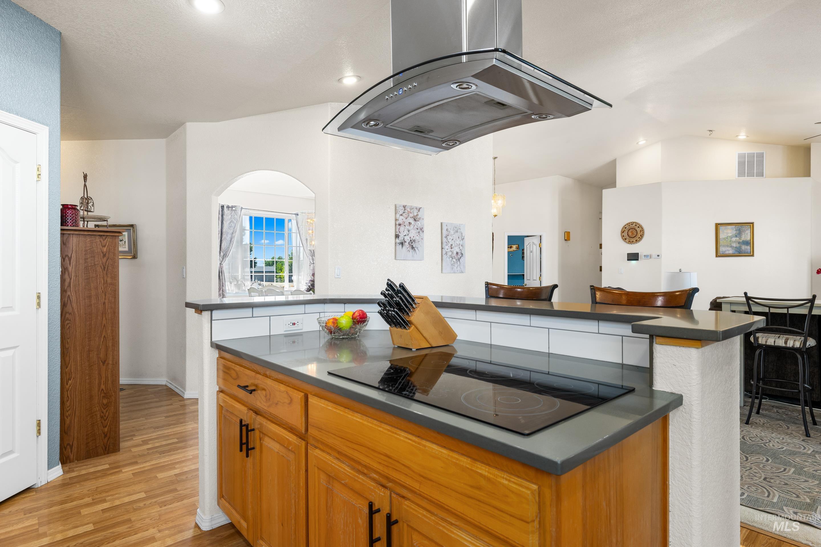 Kitchen with extractor fan, dark countertops, black electric stovetop, light wood-style flooring, and lofted ceiling