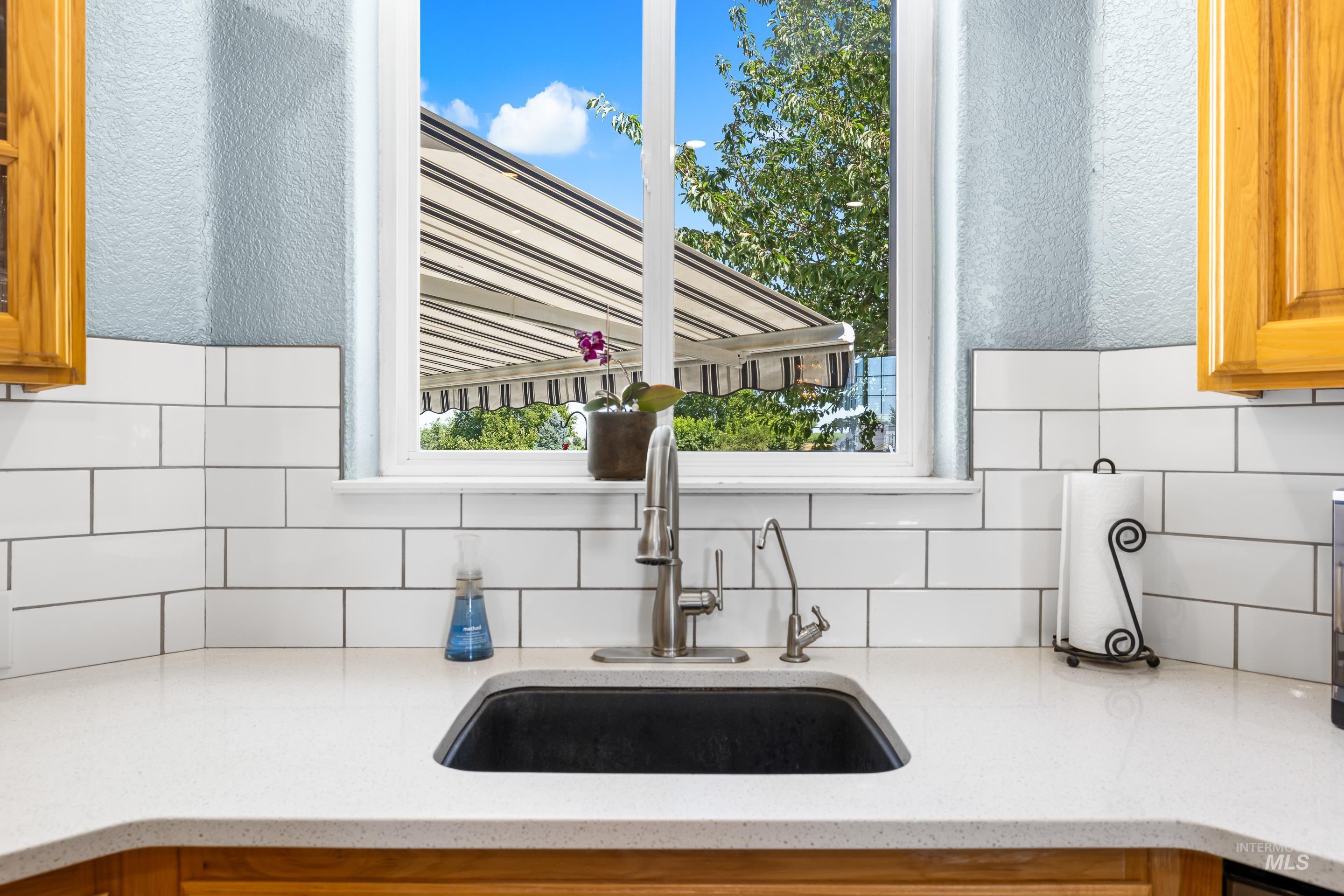 Kitchen view of backsplash, light stone counters, glass insert cabinets, and brown cabinetry