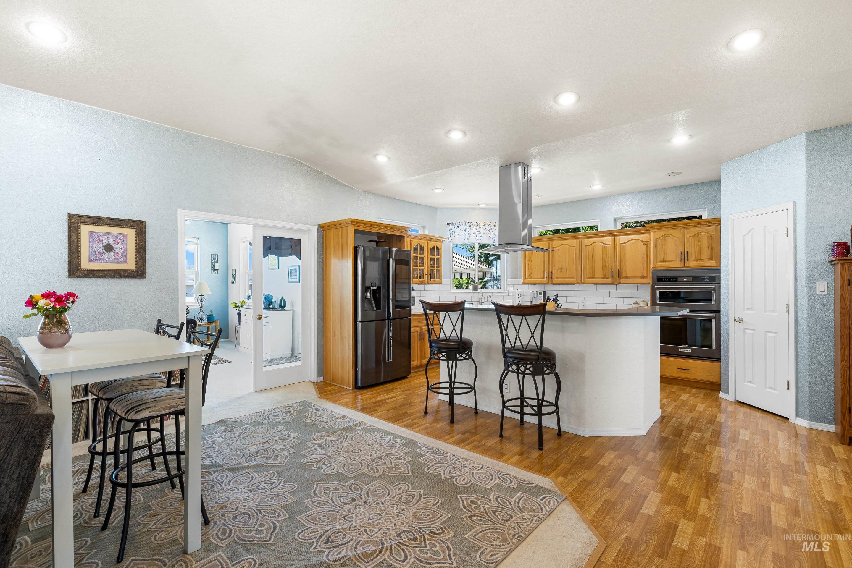 Kitchen with a kitchen breakfast bar, stainless steel fridge, light wood-style floors, island range hood, and a textured wall