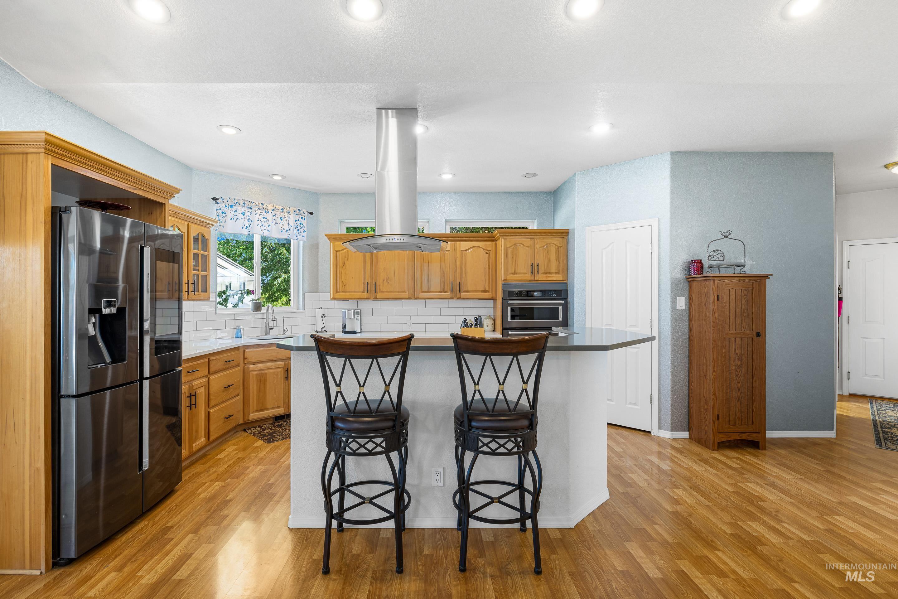 Kitchen with a kitchen breakfast bar, stainless steel fridge with ice dispenser, a center island, island exhaust hood, and light wood finished floors