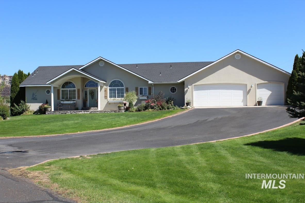 Single story home featuring stucco siding, a front yard, an attached garage, driveway, and a shingled roof