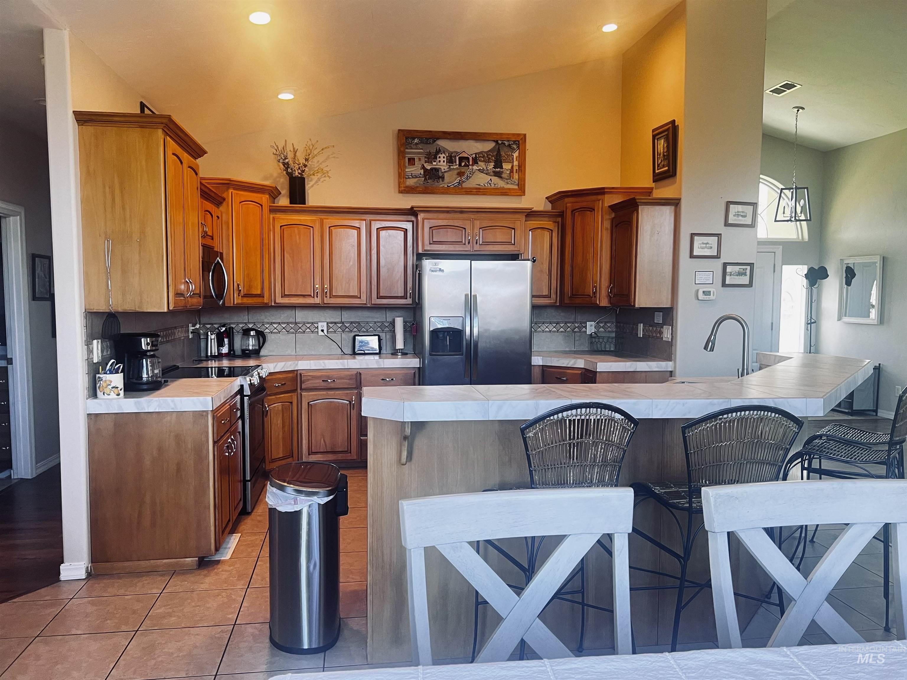 Kitchen featuring a kitchen breakfast bar, appliances with stainless steel finishes, light countertops, brown cabinets, and tasteful backsplash