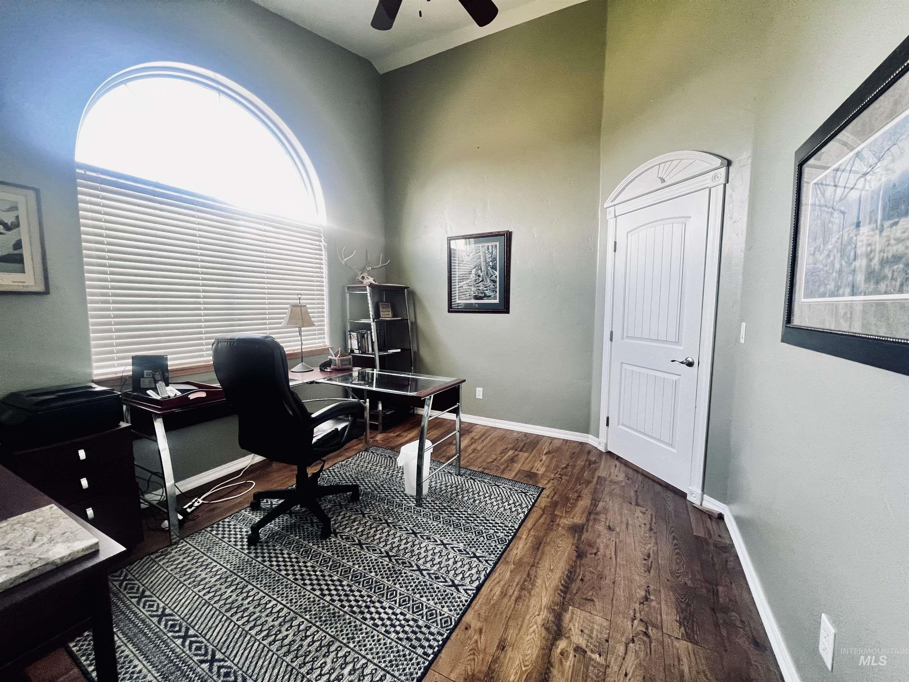 Home office featuring a ceiling fan, dark wood-style floors, and a high ceiling