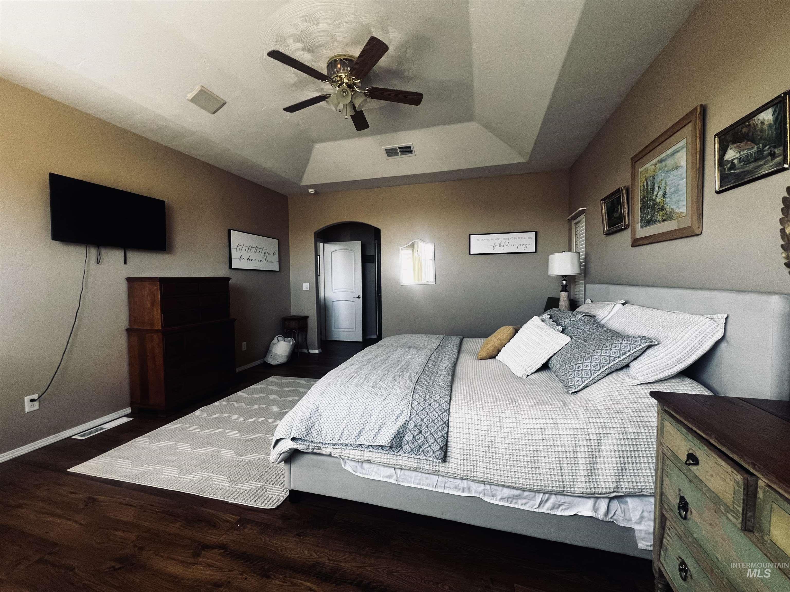 Bedroom featuring a raised ceiling, dark wood-type flooring, ceiling fan, and arched walkways
