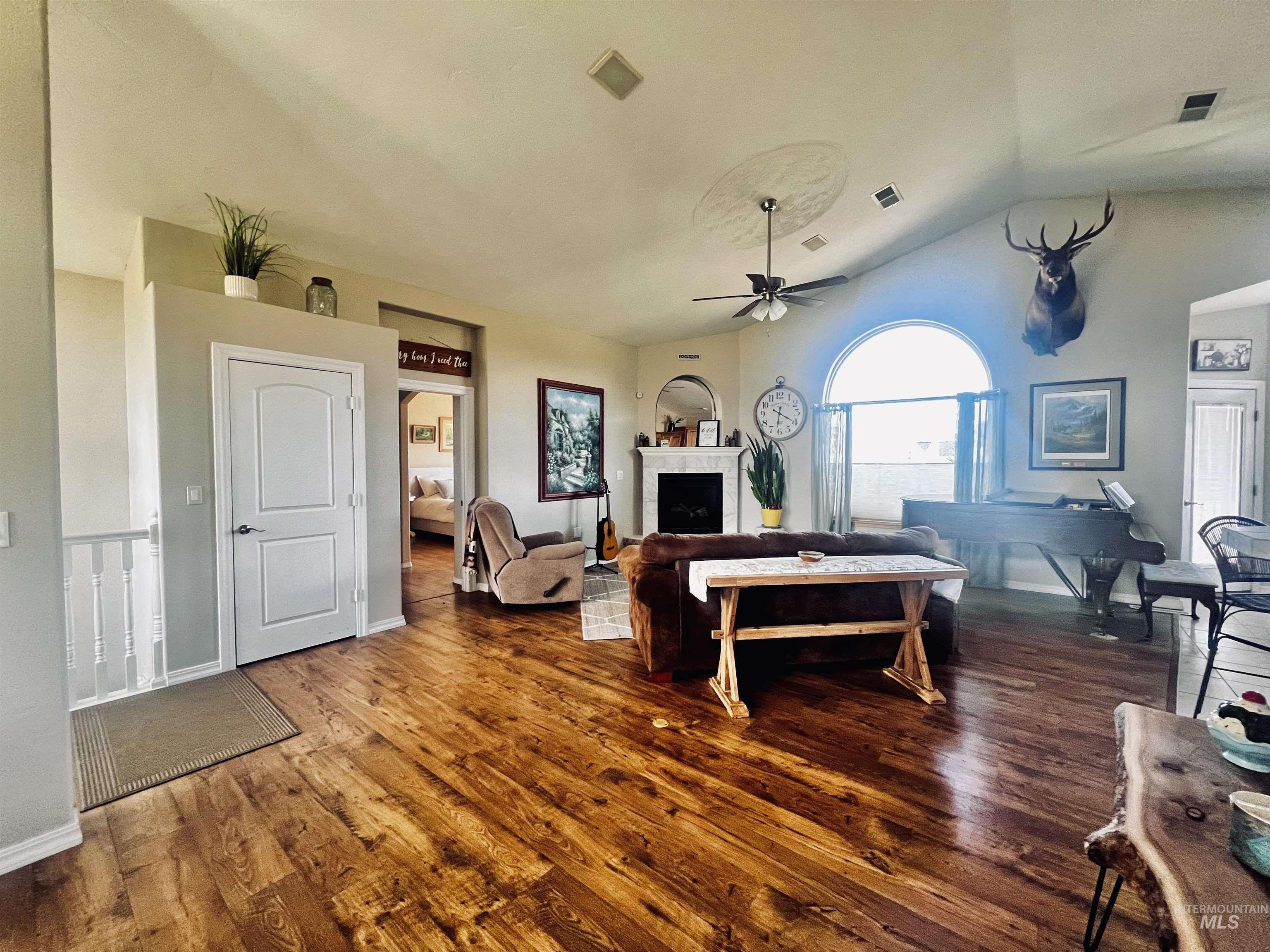 Living area featuring a fireplace, dark wood-type flooring, lofted ceiling, and a ceiling fan