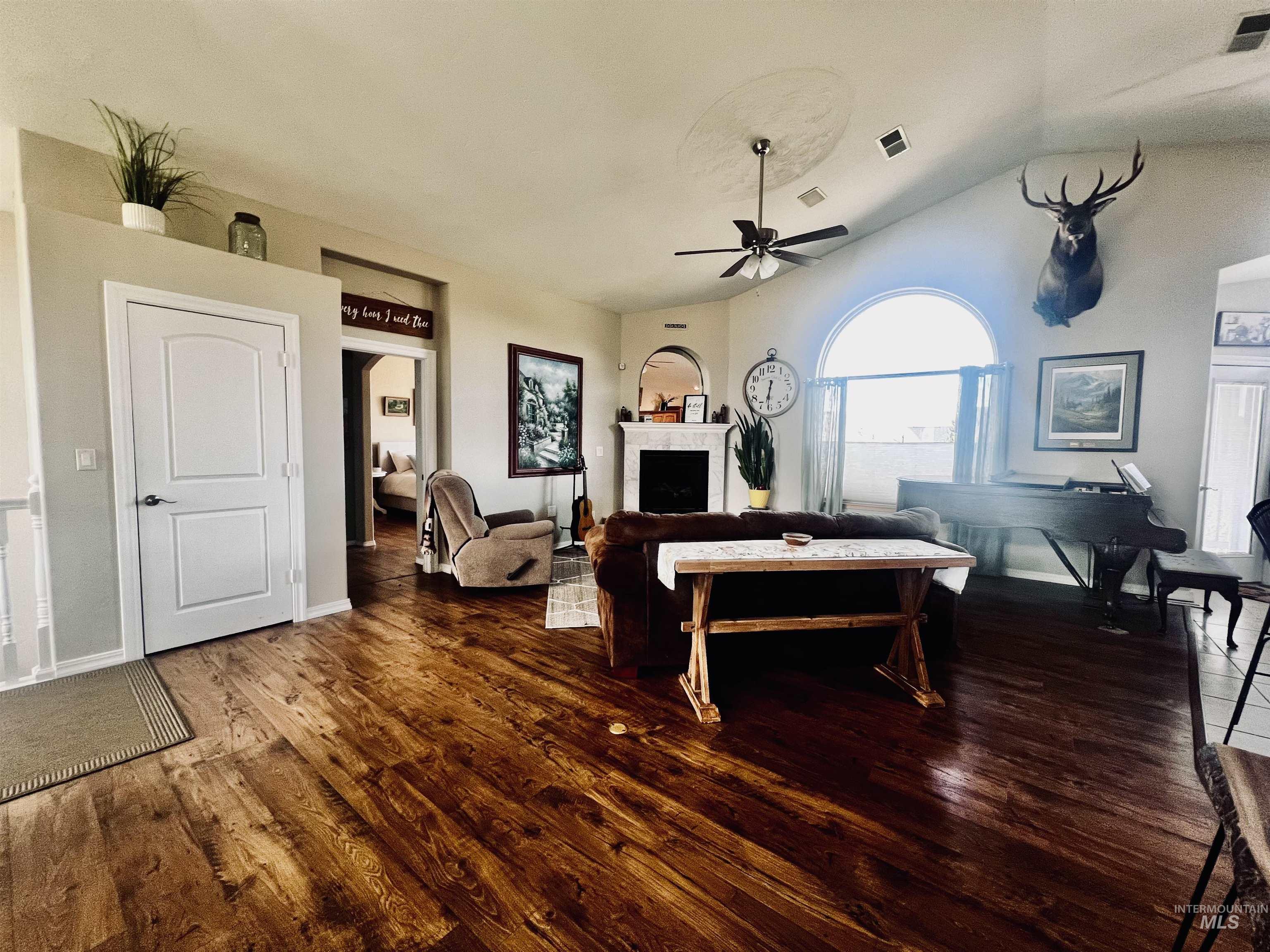Living room with a fireplace, dark wood-style floors, vaulted ceiling, and ceiling fan