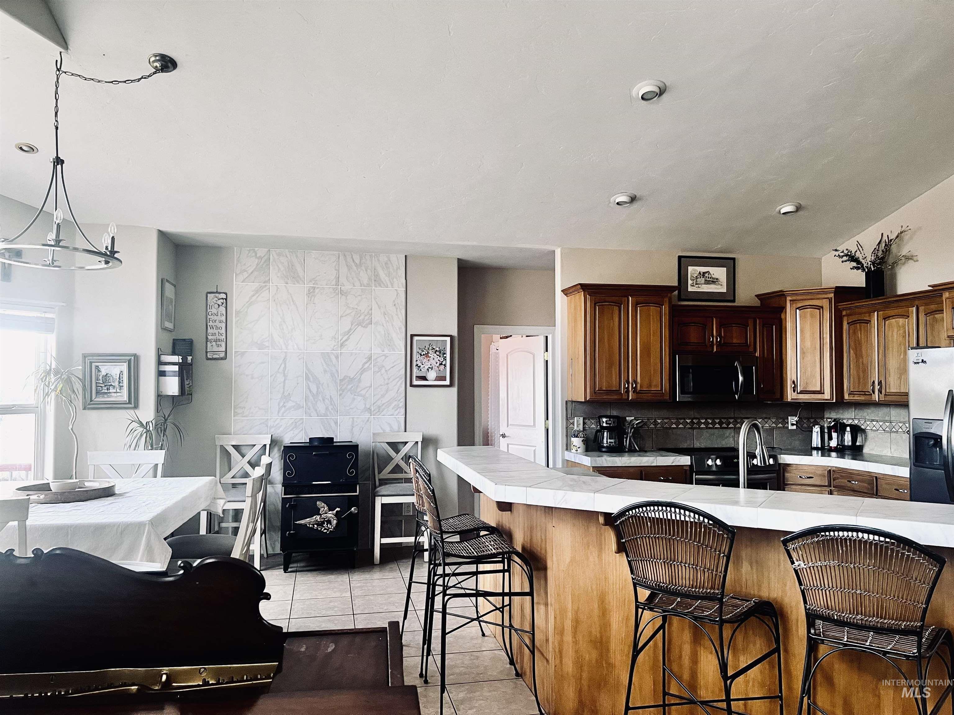 Kitchen with light tile patterned flooring, a kitchen breakfast bar, appliances with stainless steel finishes, hanging light fixtures, and tasteful backsplash