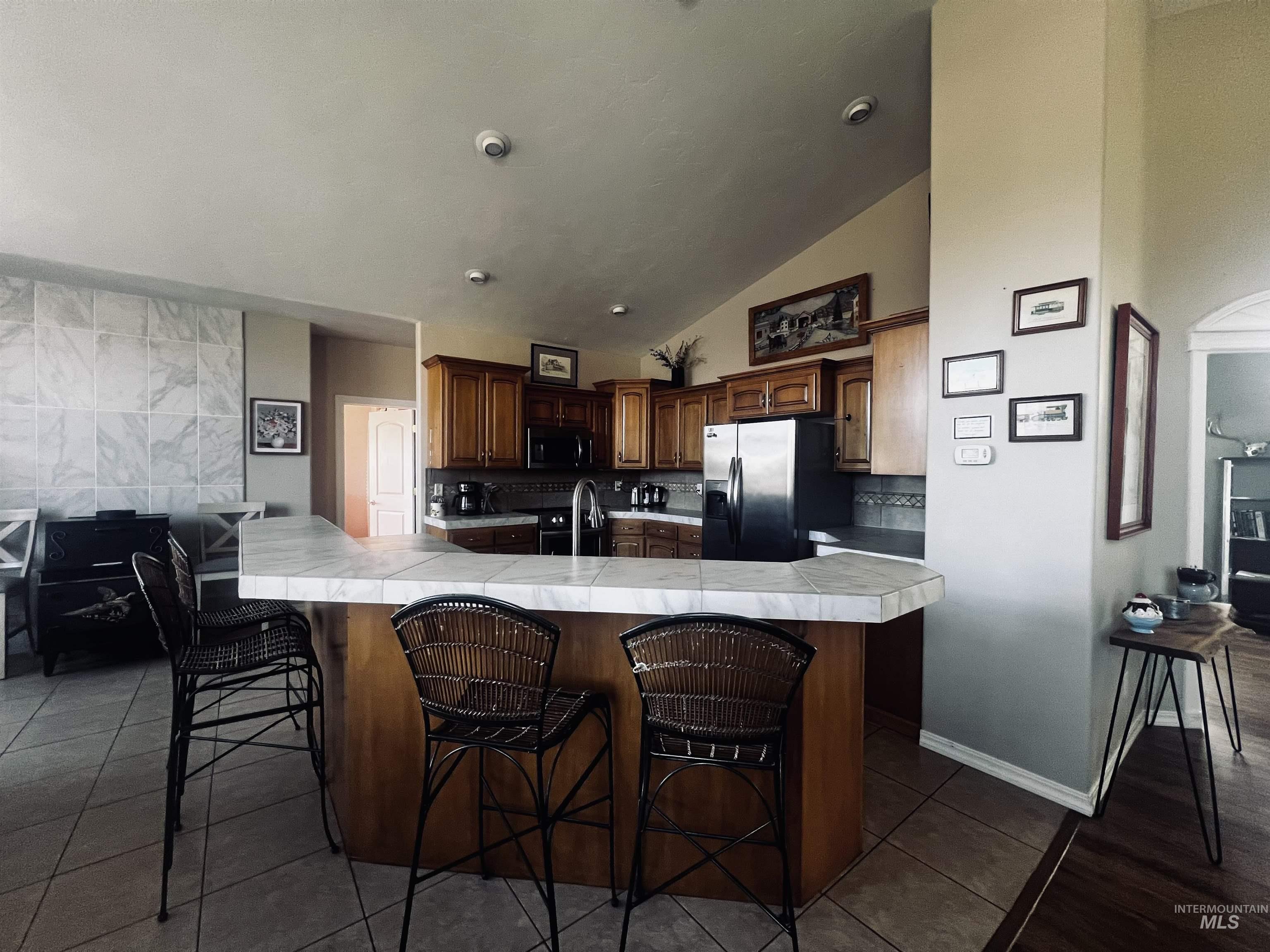 Kitchen featuring appliances with stainless steel finishes, a kitchen bar, dark tile patterned flooring, lofted ceiling, and tasteful backsplash